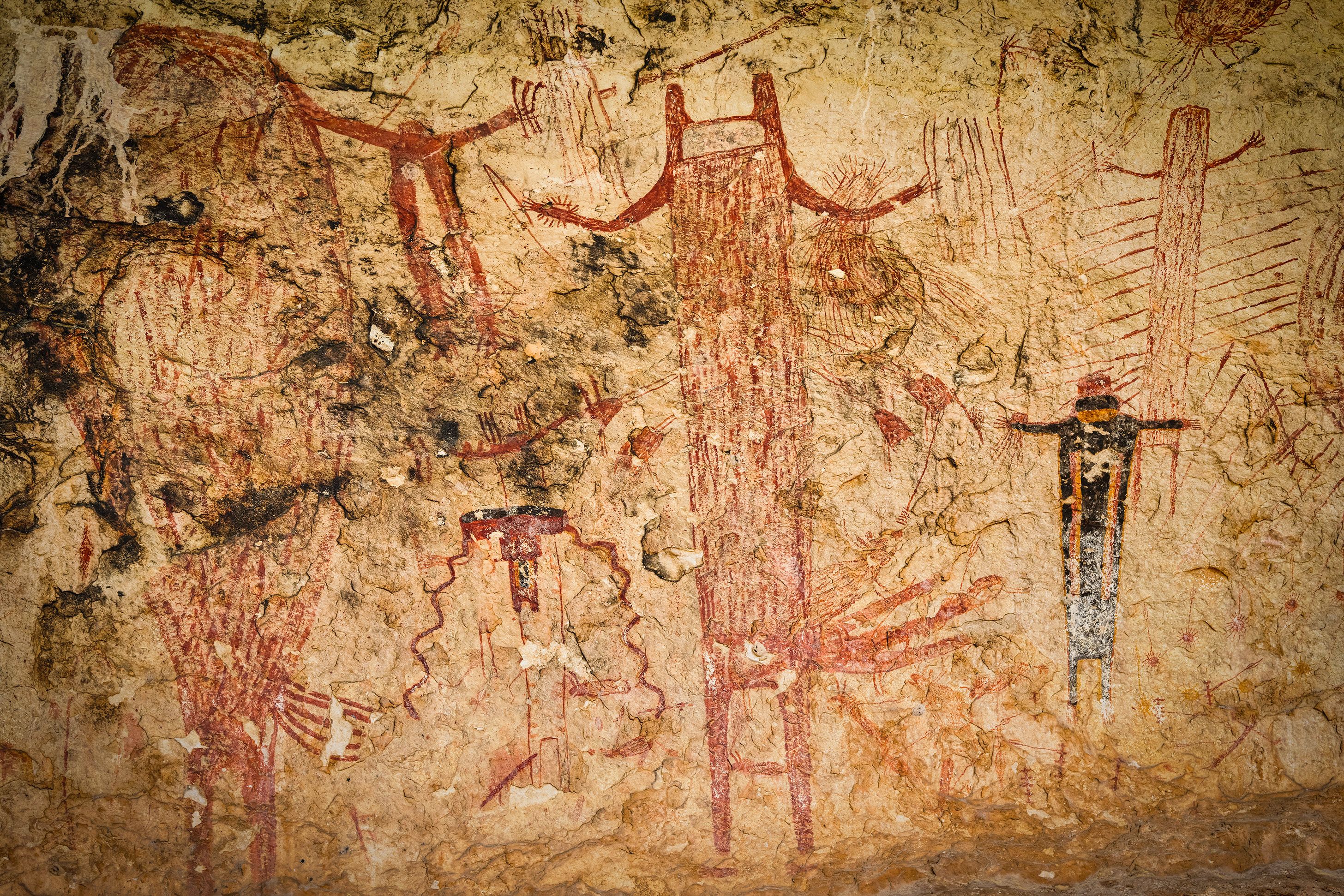 Ancient rock painting showing humanoid figures with arms outstretched on a weathered stone surface.