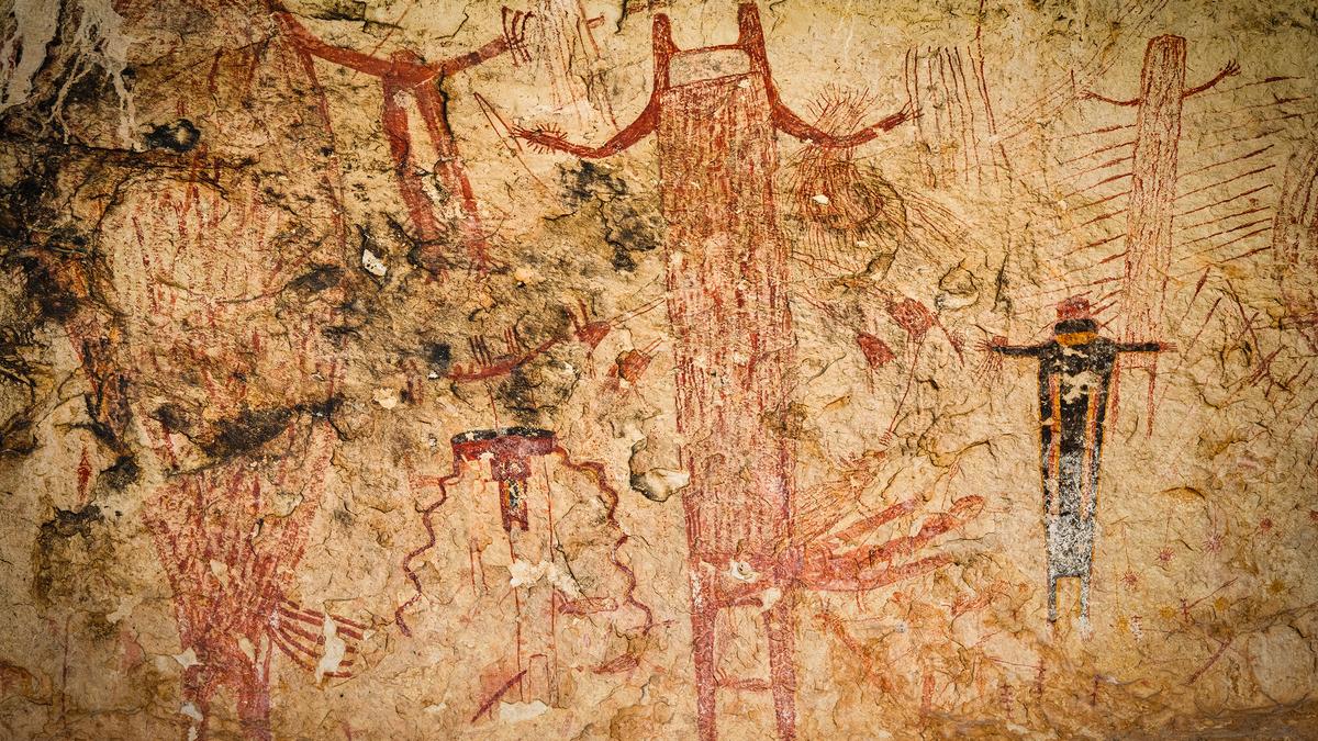 Ancient rock painting showing humanoid figures with arms outstretched on a weathered stone surface.