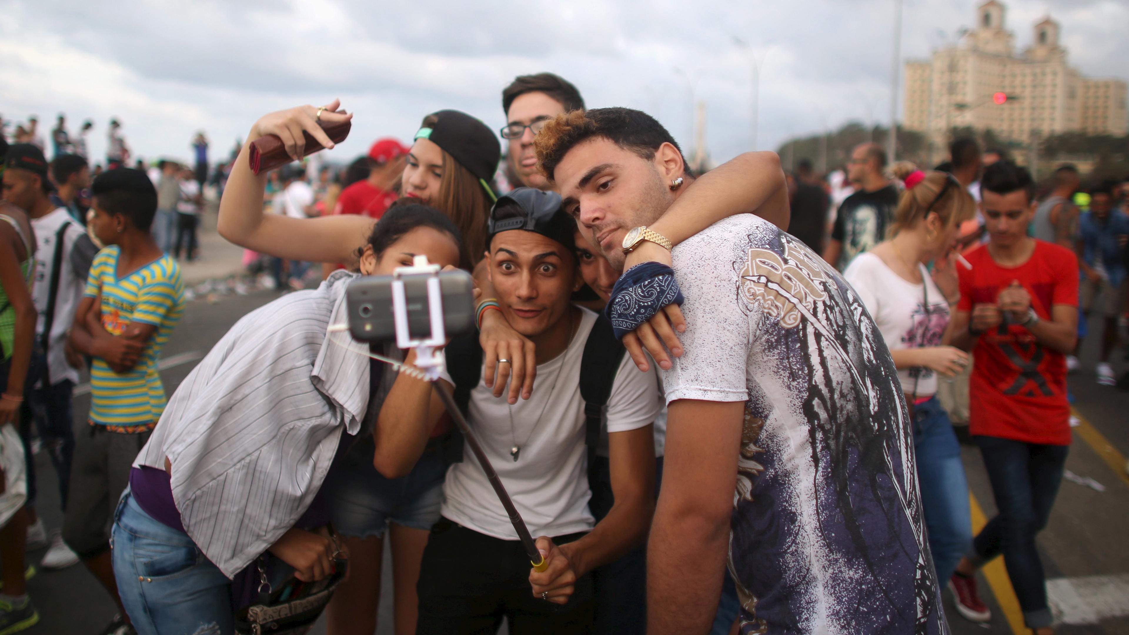 Photo of a group of young people taking a selfie with a smartphone outdoors in a busy urban setting.