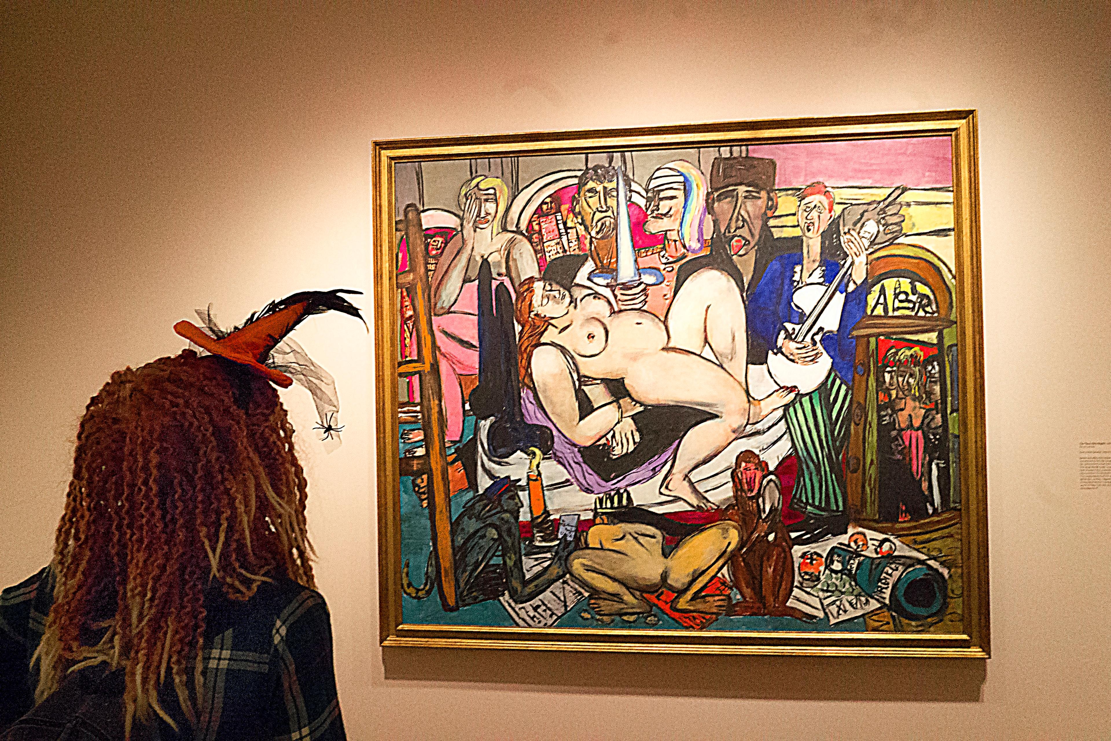 Person in a hat with feathers admires a colourful painting in a gallery.