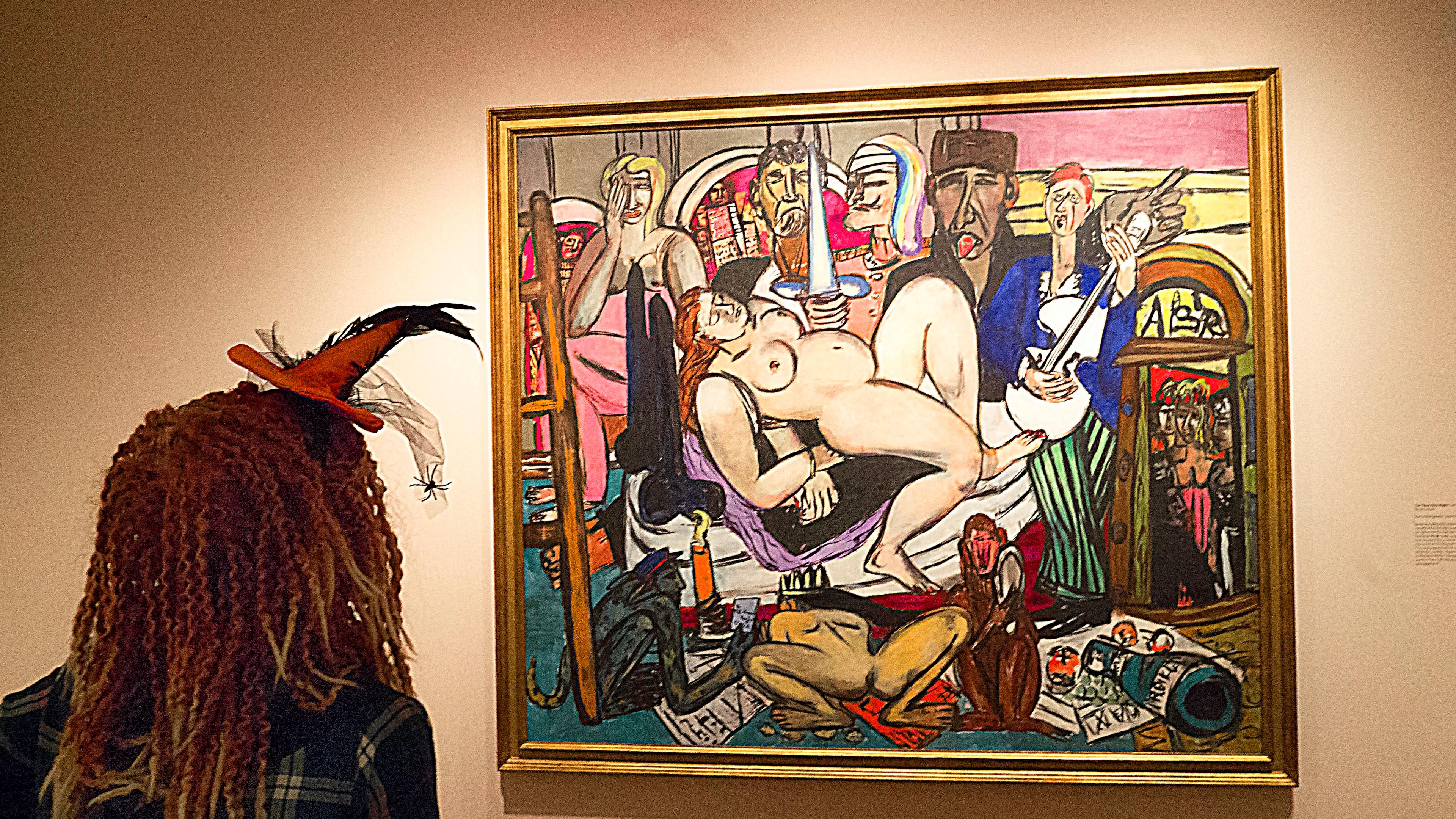 Person in a hat with feathers admires a colourful painting in a gallery.