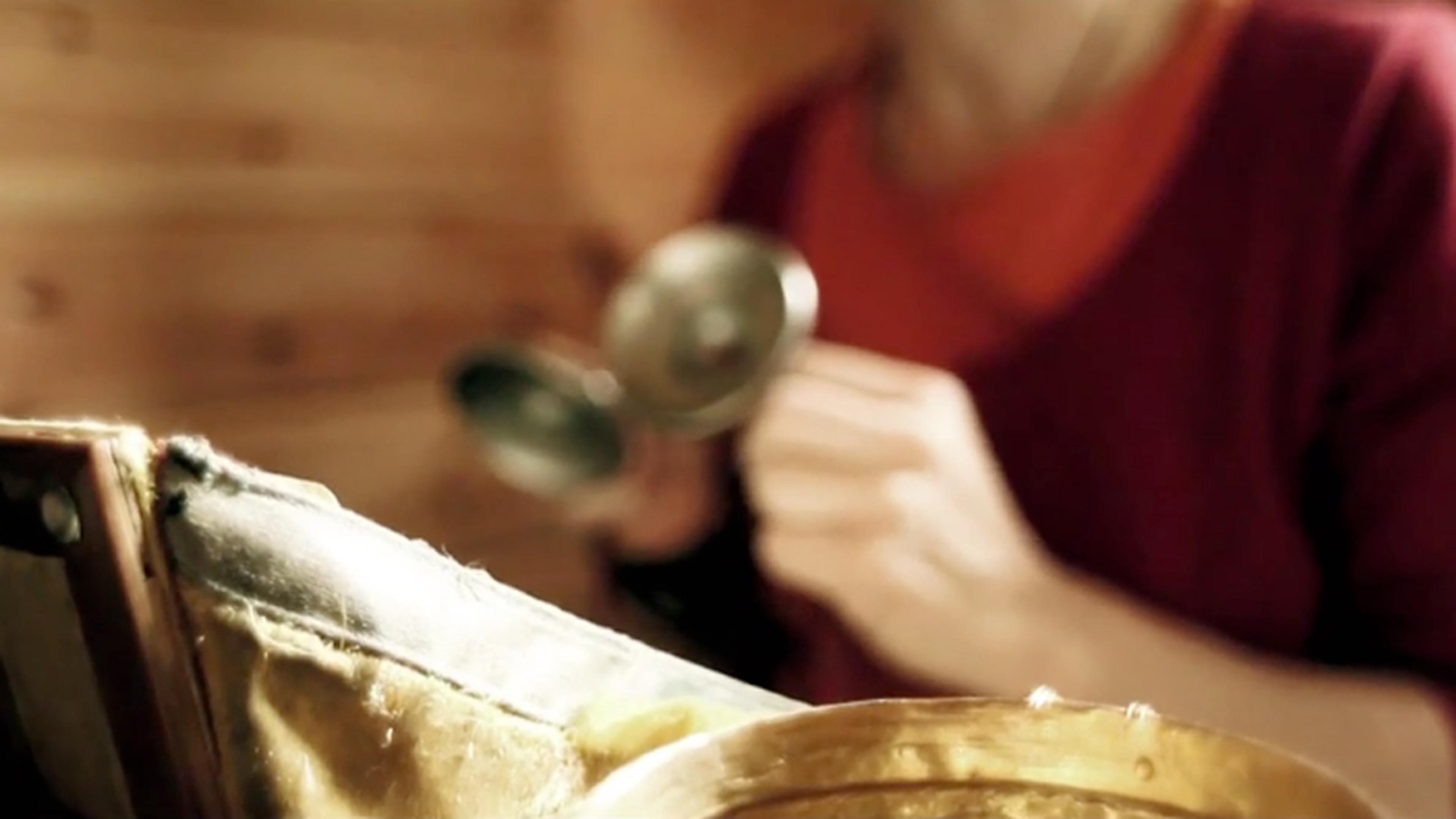 A blurred photo of a person in a red shirt holding metal objects, with a focus on a close-up of a leather-bound machinery part.