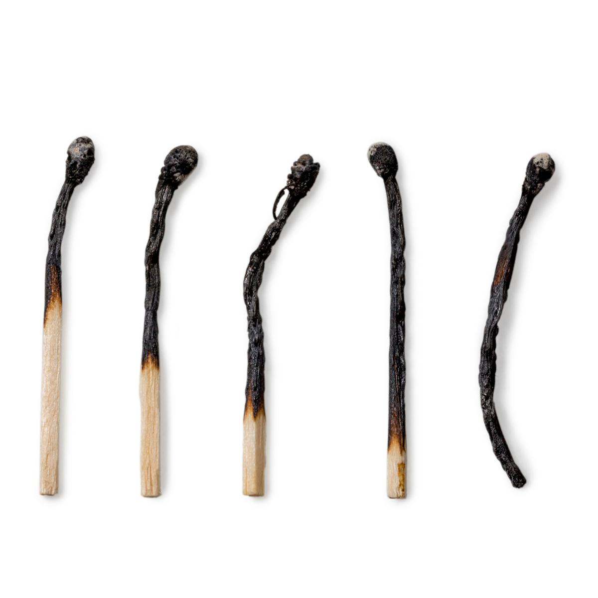 Photo of five burned matchsticks with blackened, charred tips, arranged in a row on a white background. The order shows partially burnt matches through to a fully burnt match.