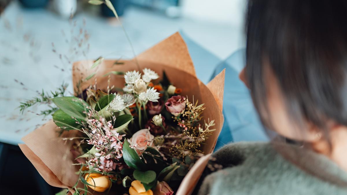 A photo showing a person holding a bouquet of mixed flowers wrapped in brown paper, viewed from above and behind.