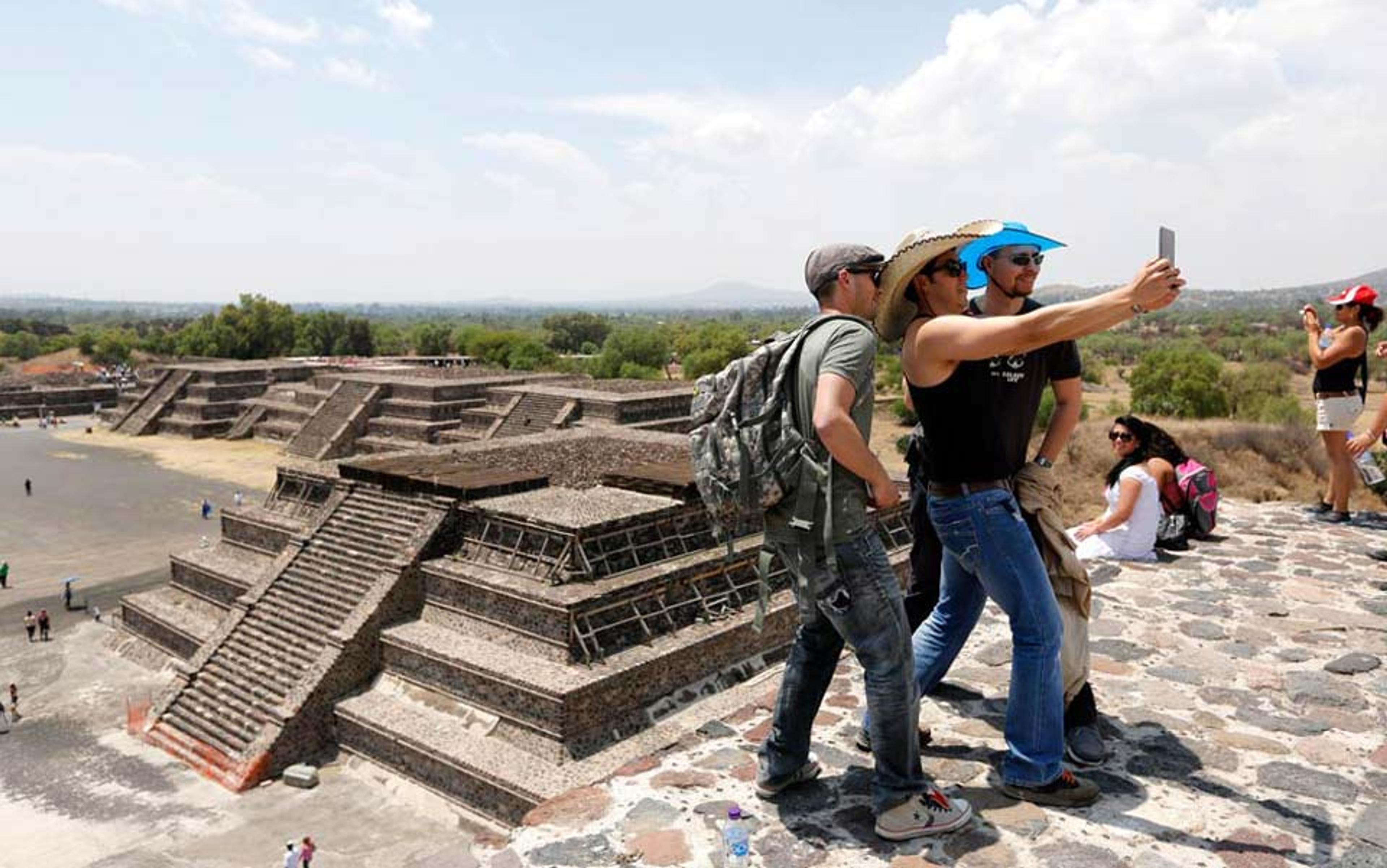 Three tourists in sunhats taking a selfie at the pyramids with other visitors and a green landscape in the background