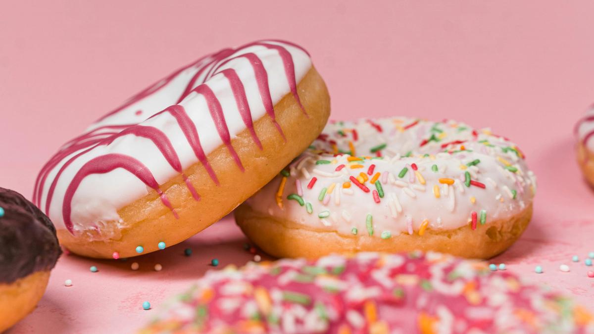 Photo of doughnuts with white icing and colourful sprinkles on a pink background.