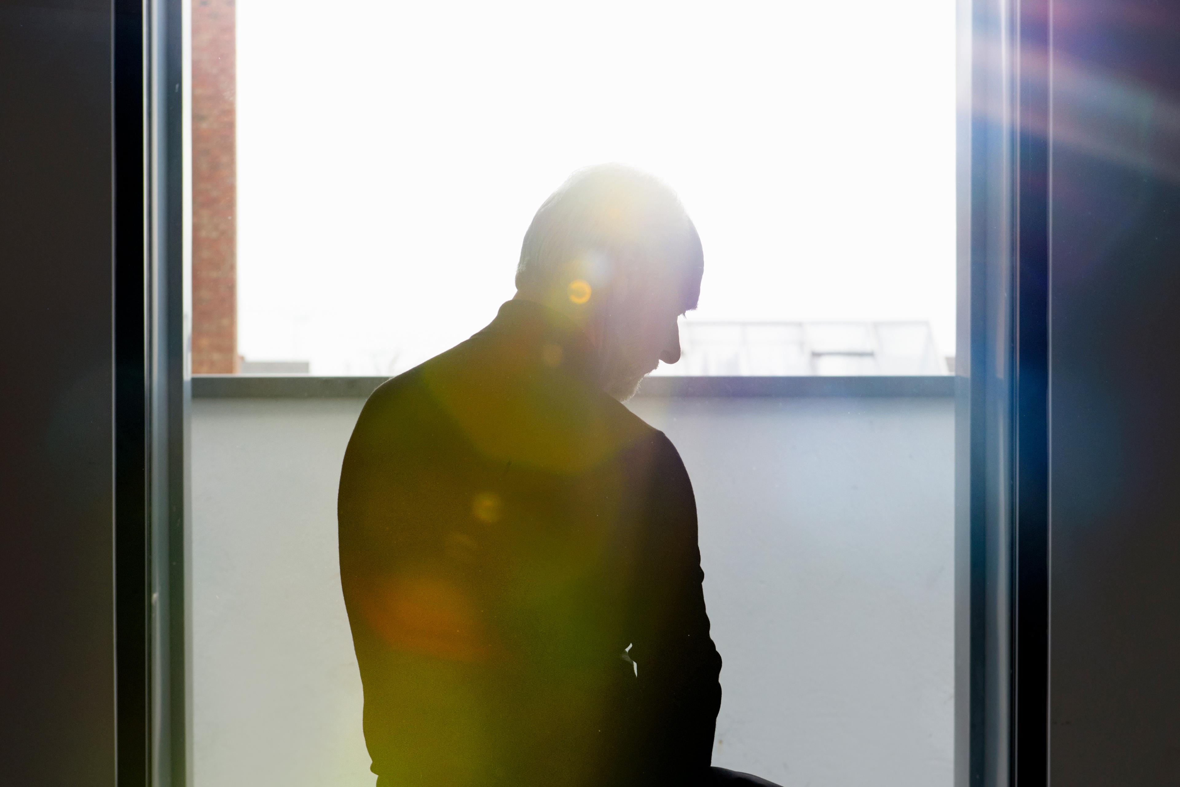 Silhouette of a person sitting against a bright window with lens flare effects and a partial view of the outside city.