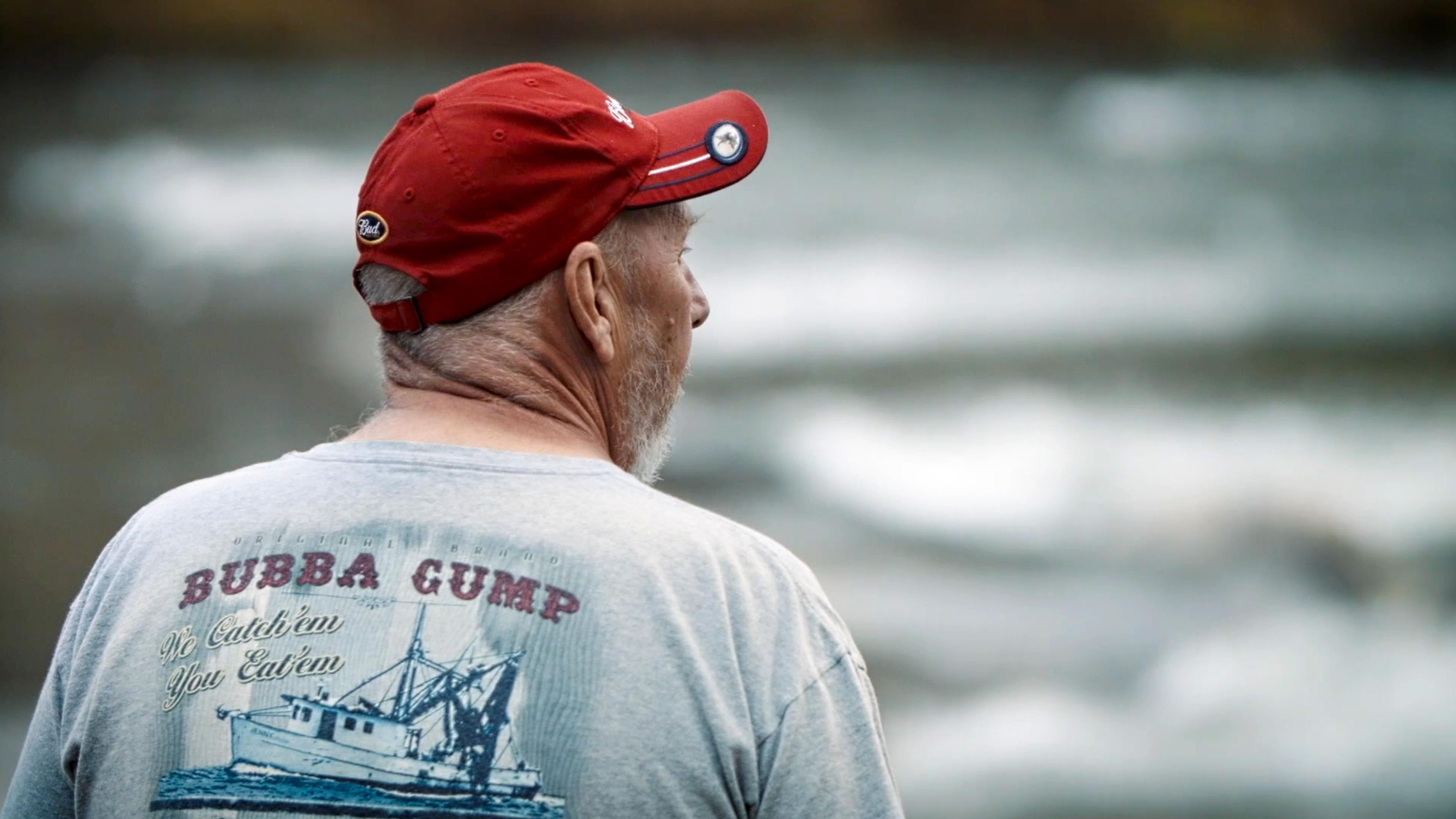 An older man in a red cap and printed T-shirt looking into the distance.