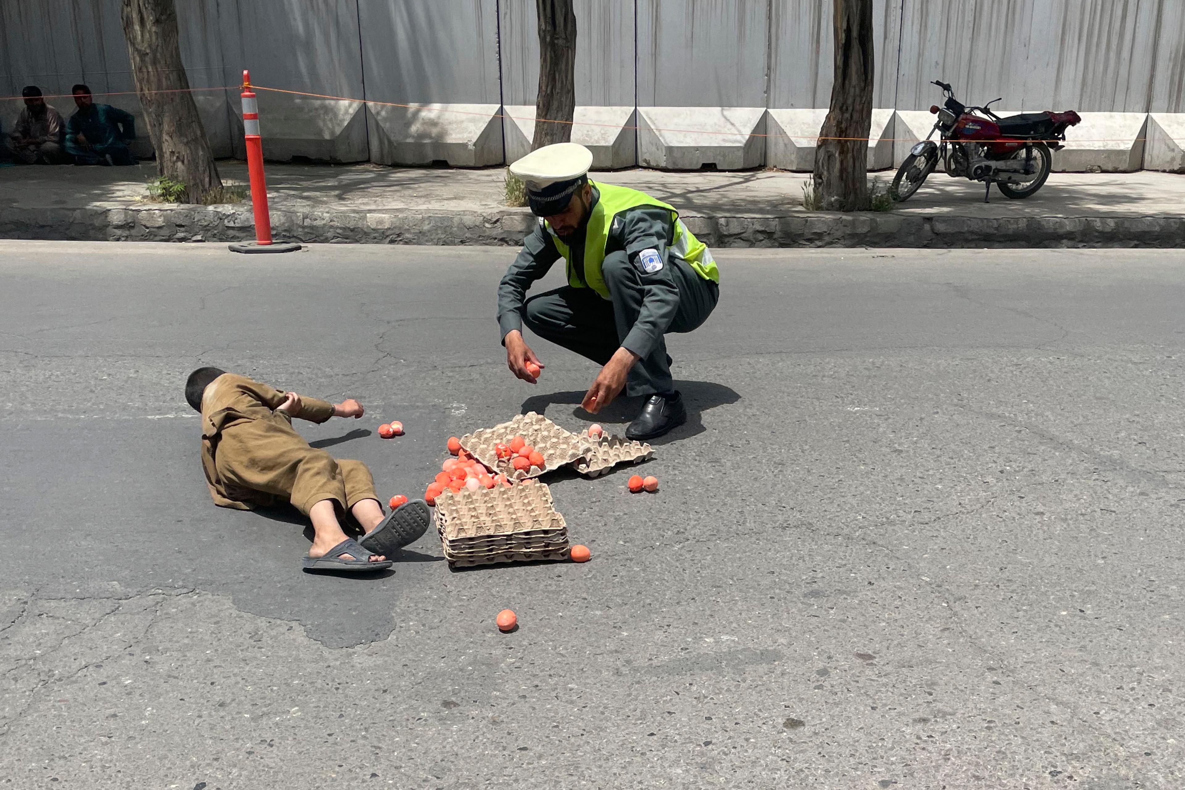 Photo of a policeman helping a child on the road with spilled eggs from cartons next to a motorcycle.