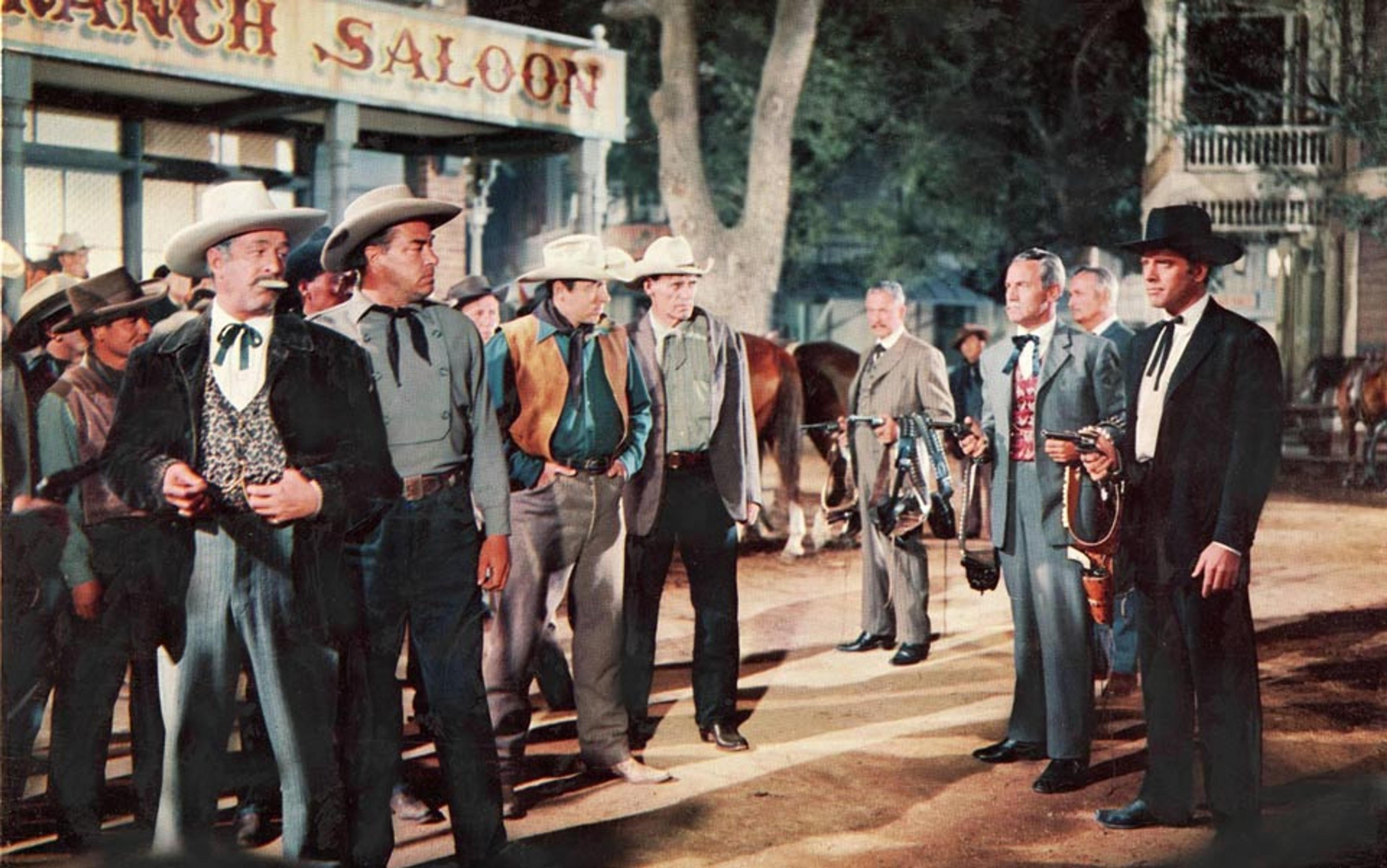 Film still of a group of men in Western attire standing outside Ranch Saloon in a historical town setting, some holding weapons.