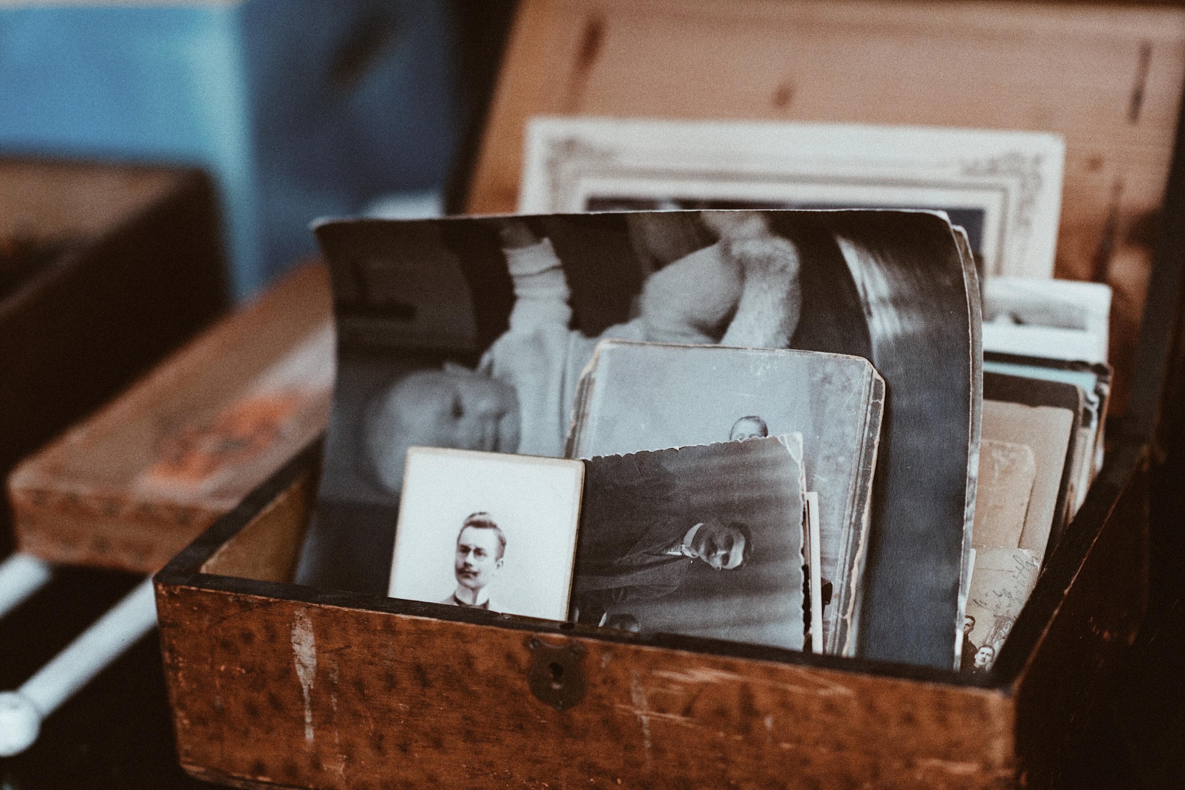 A wooden box filled with vintage black-and-white photos, some faded, shown in an artistic photograph.