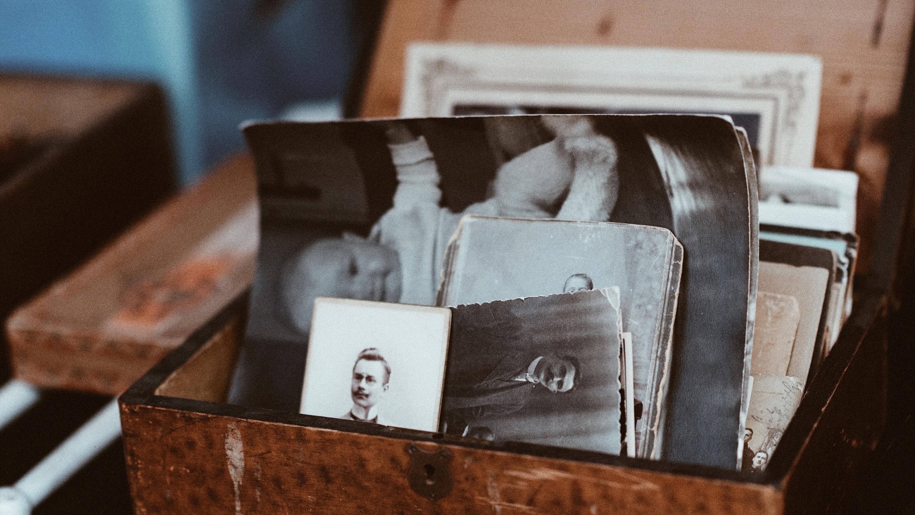 A wooden box filled with vintage black-and-white photos, some faded, shown in an artistic photograph.