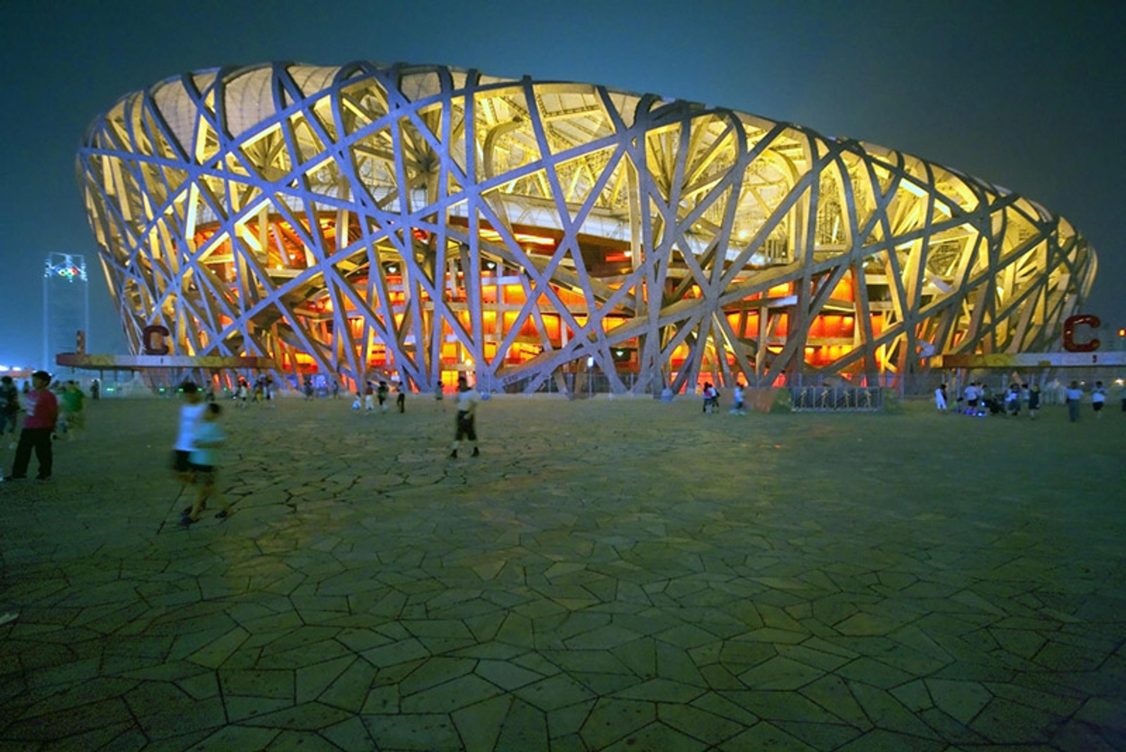 The Bird’s Nest stadium in Beijing at night, with its illuminated architectural design and people walking in the foreground.