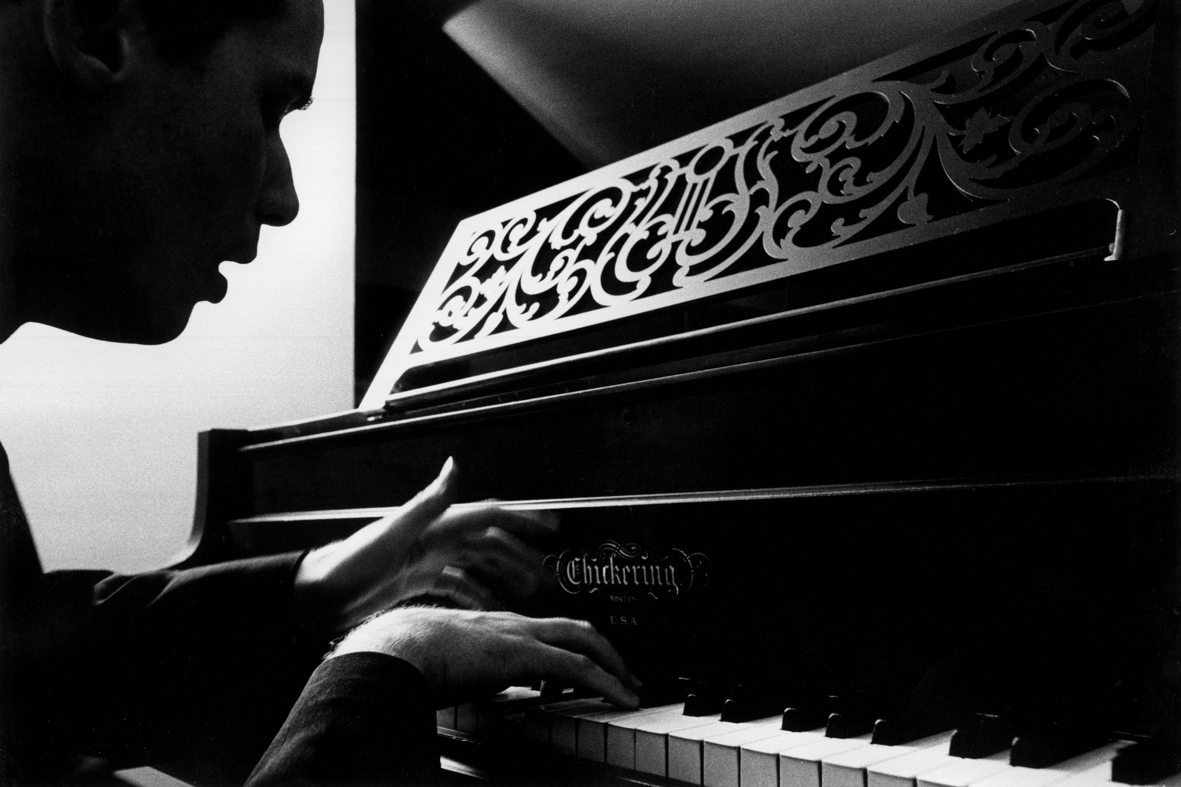 Black and white photo of a person playing a piano with an ornate music stand.