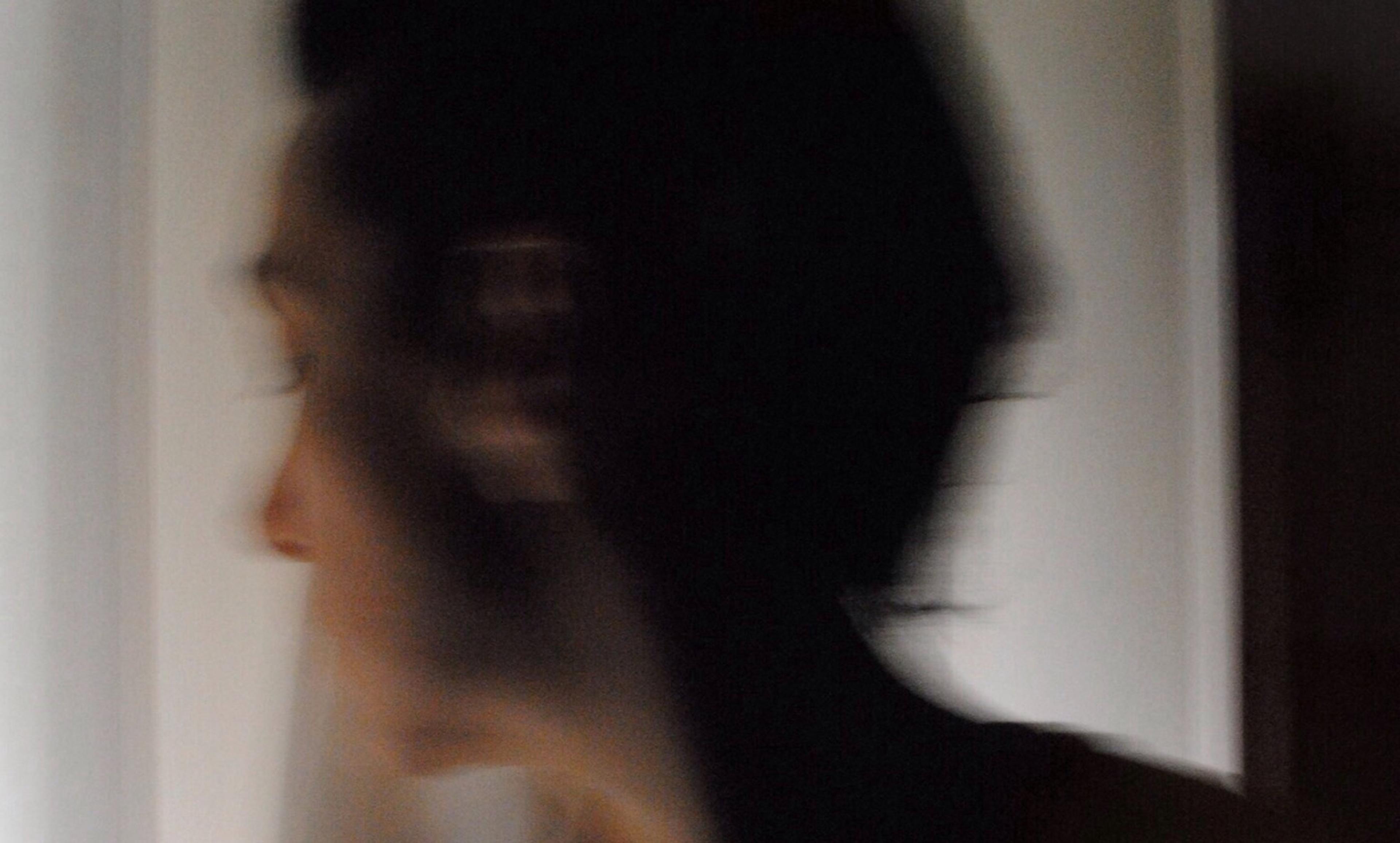 A blurred person with dark hair looking to the left, background mostly white and out of focus.