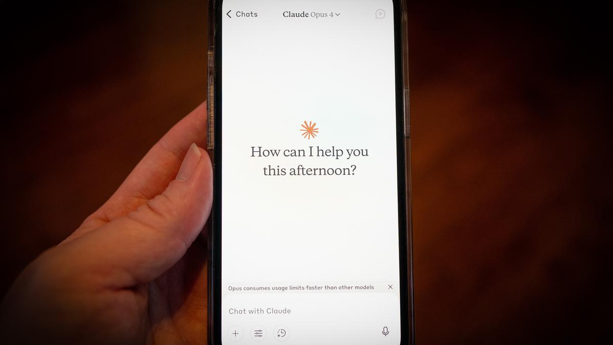 Photo of a hand holding a smartphone displaying a chat app interface asking “How can I help you this afternoon?”