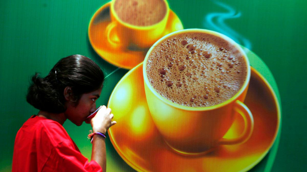 A person drinking next to a large poster depicting steaming coffee cups on a green background.