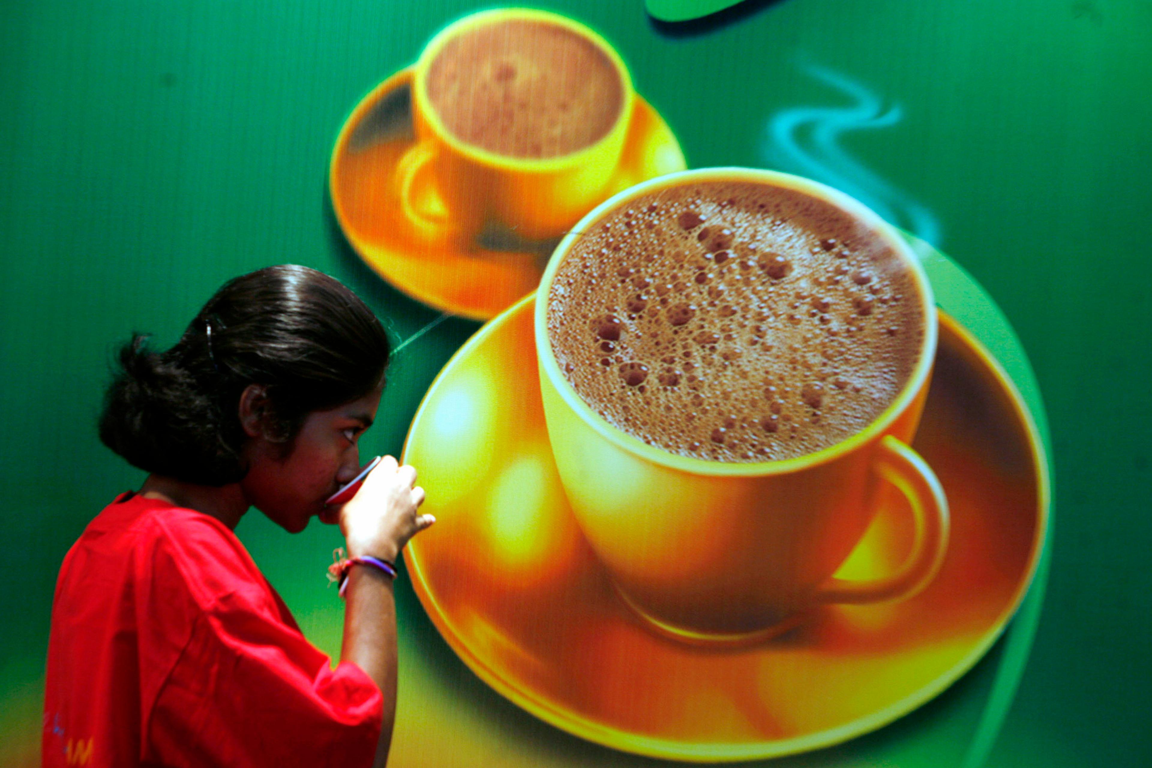 A person drinking next to a large poster depicting steaming coffee cups on a green background.