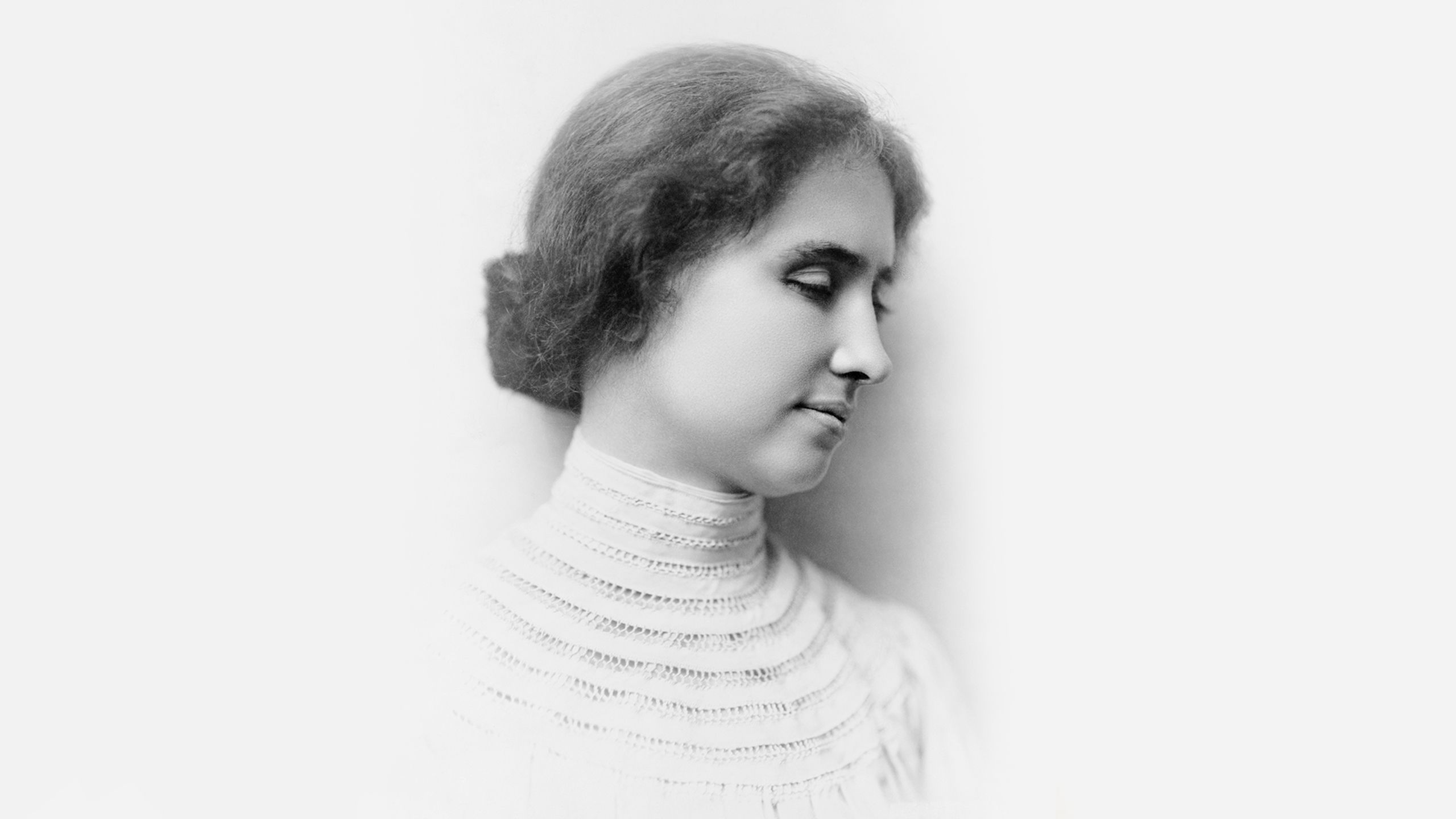 Black-and-white vintage photo of Helen Keller in profile with eyes closed wearing a high-necked dress, hair in a bun.