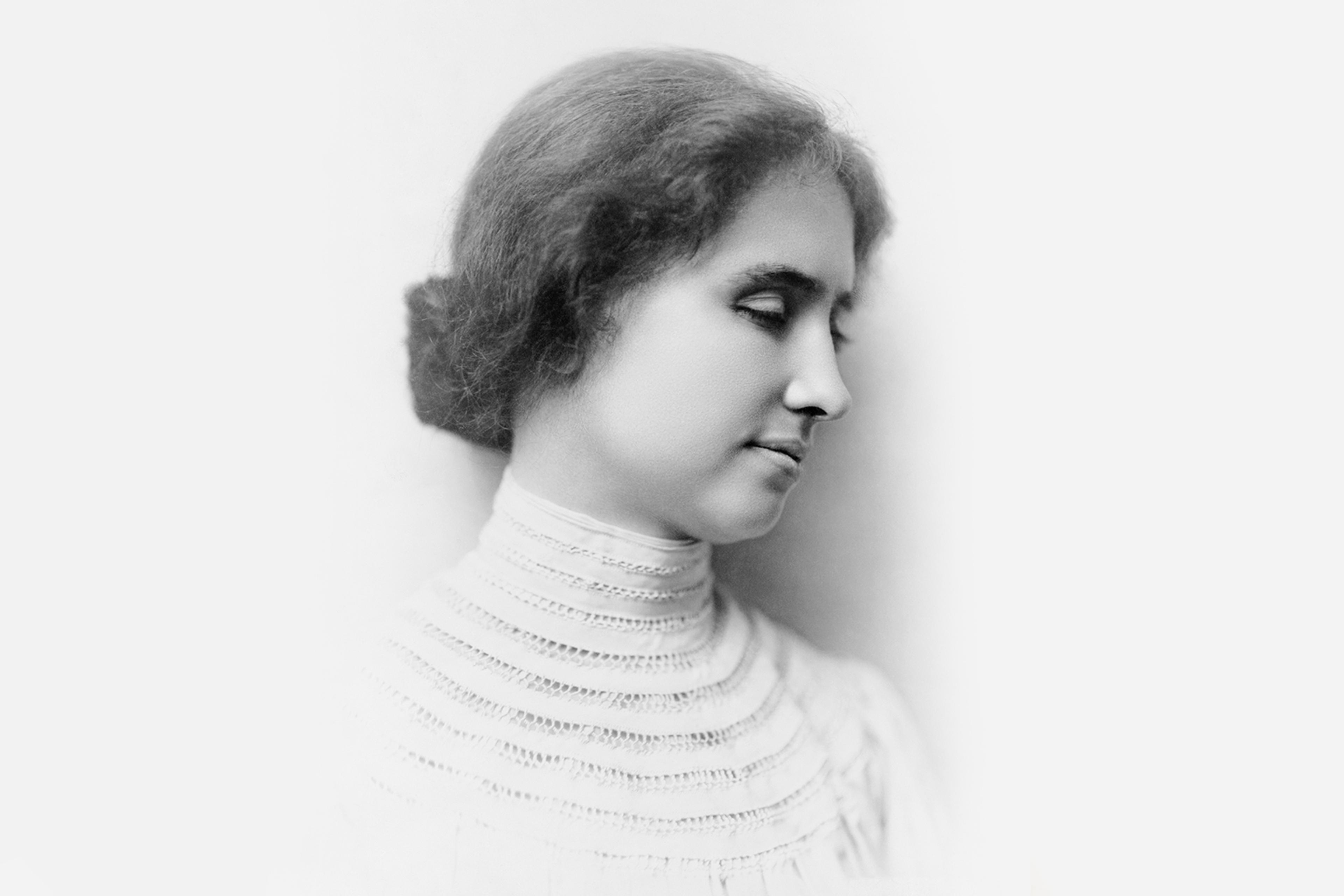 Black-and-white vintage photo of Helen Keller in profile with eyes closed wearing a high-necked dress, hair in a bun.