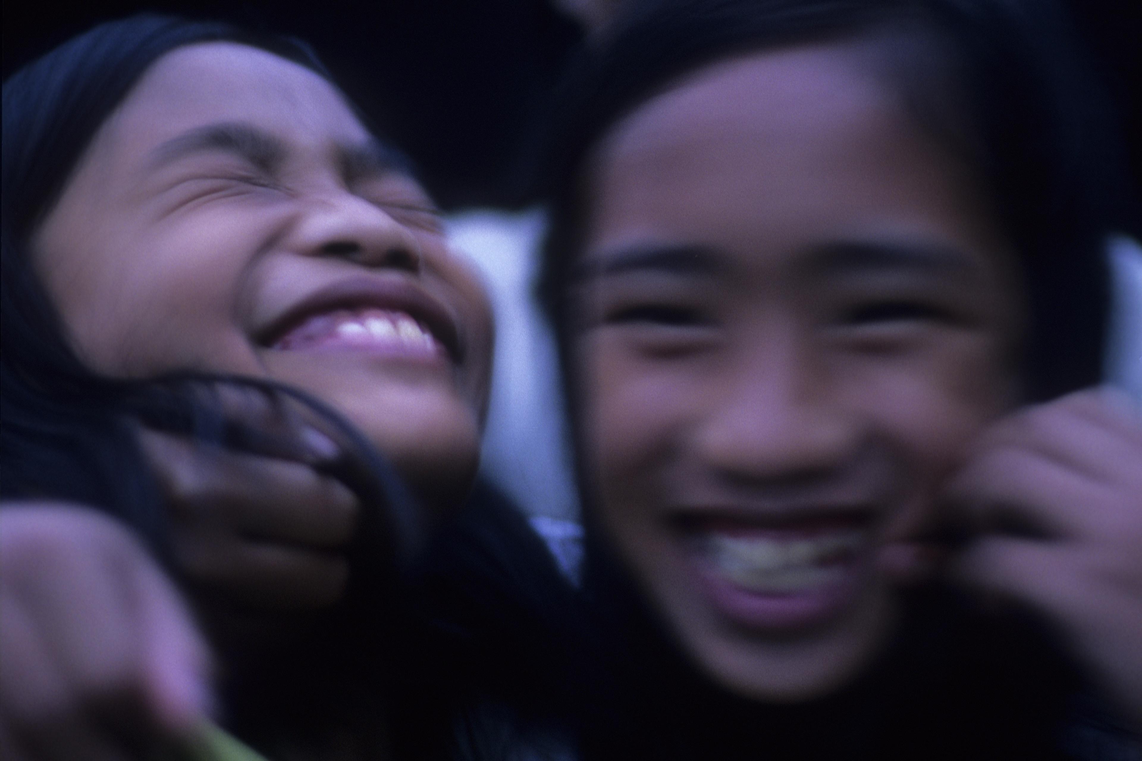 A candid photo of three smiling children slightly out of focus, showing joy and togetherness against a dark backdrop.