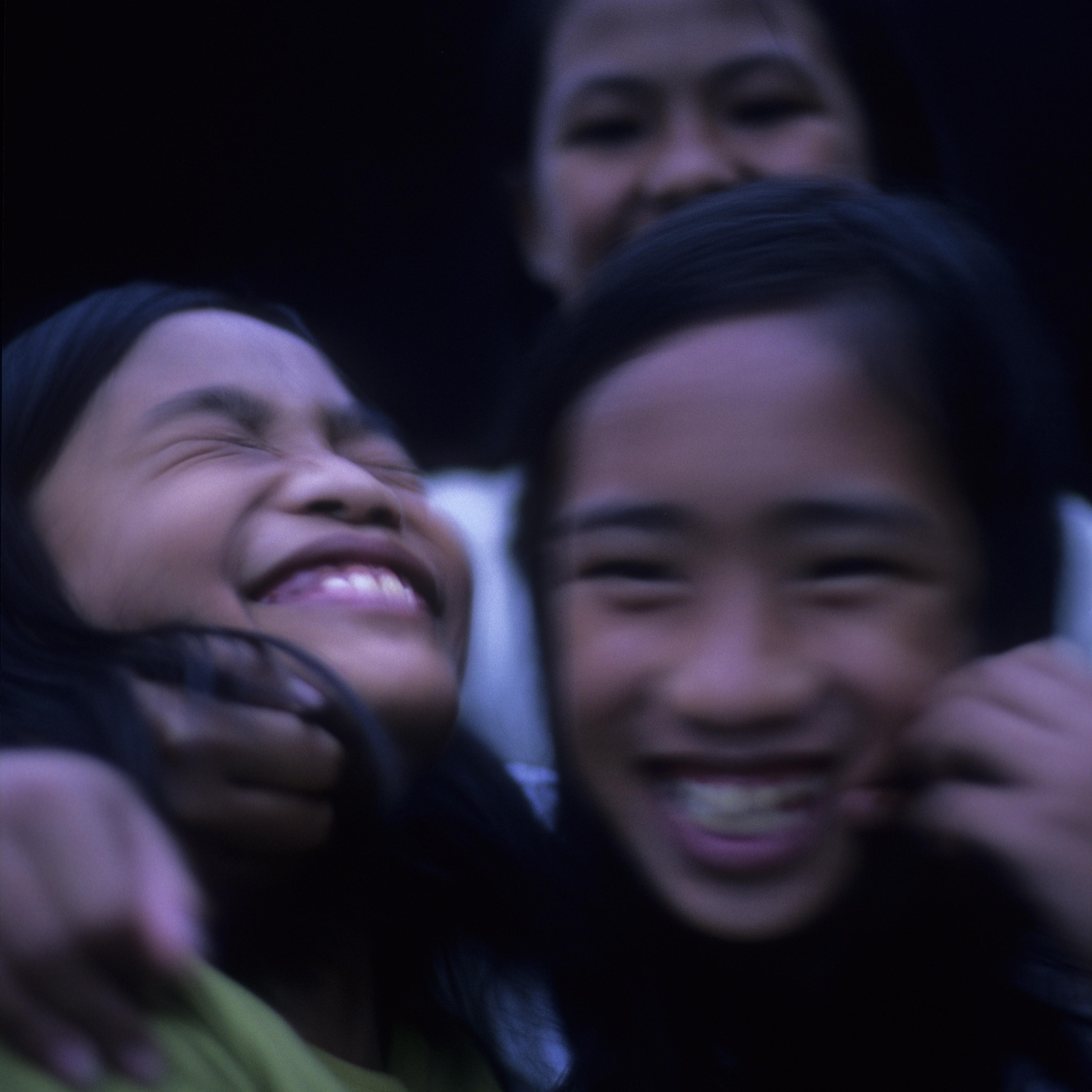 A candid photo of three smiling children slightly out of focus, showing joy and togetherness against a dark backdrop.