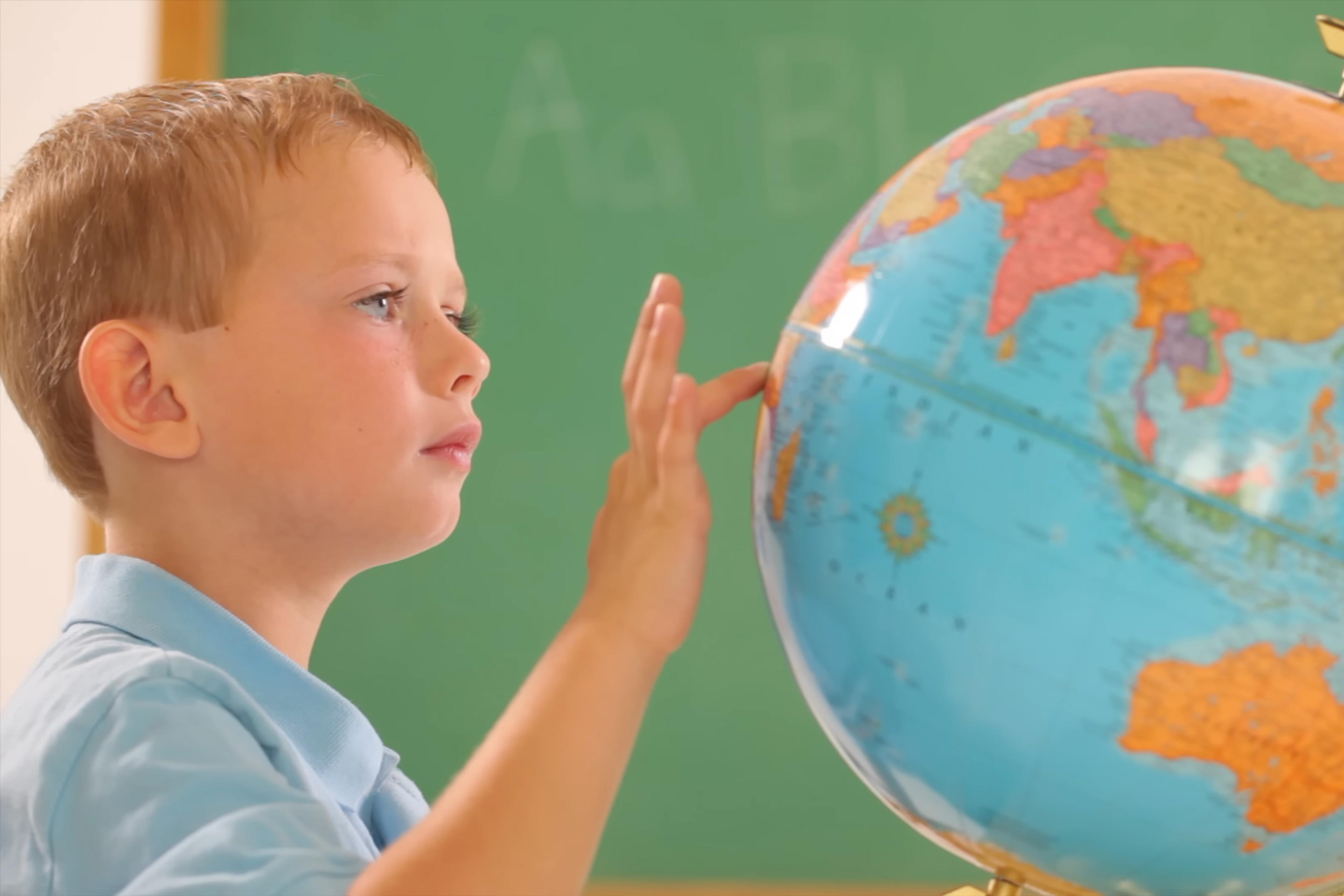 Photo of a young child in a classroom touching a globe with a chalkboard in the background.