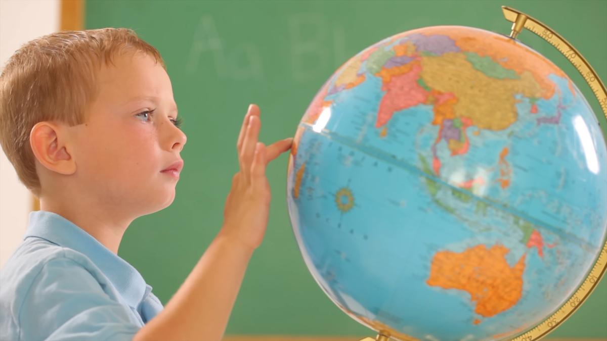 Photo of a young child in a classroom touching a globe with a chalkboard in the background.
