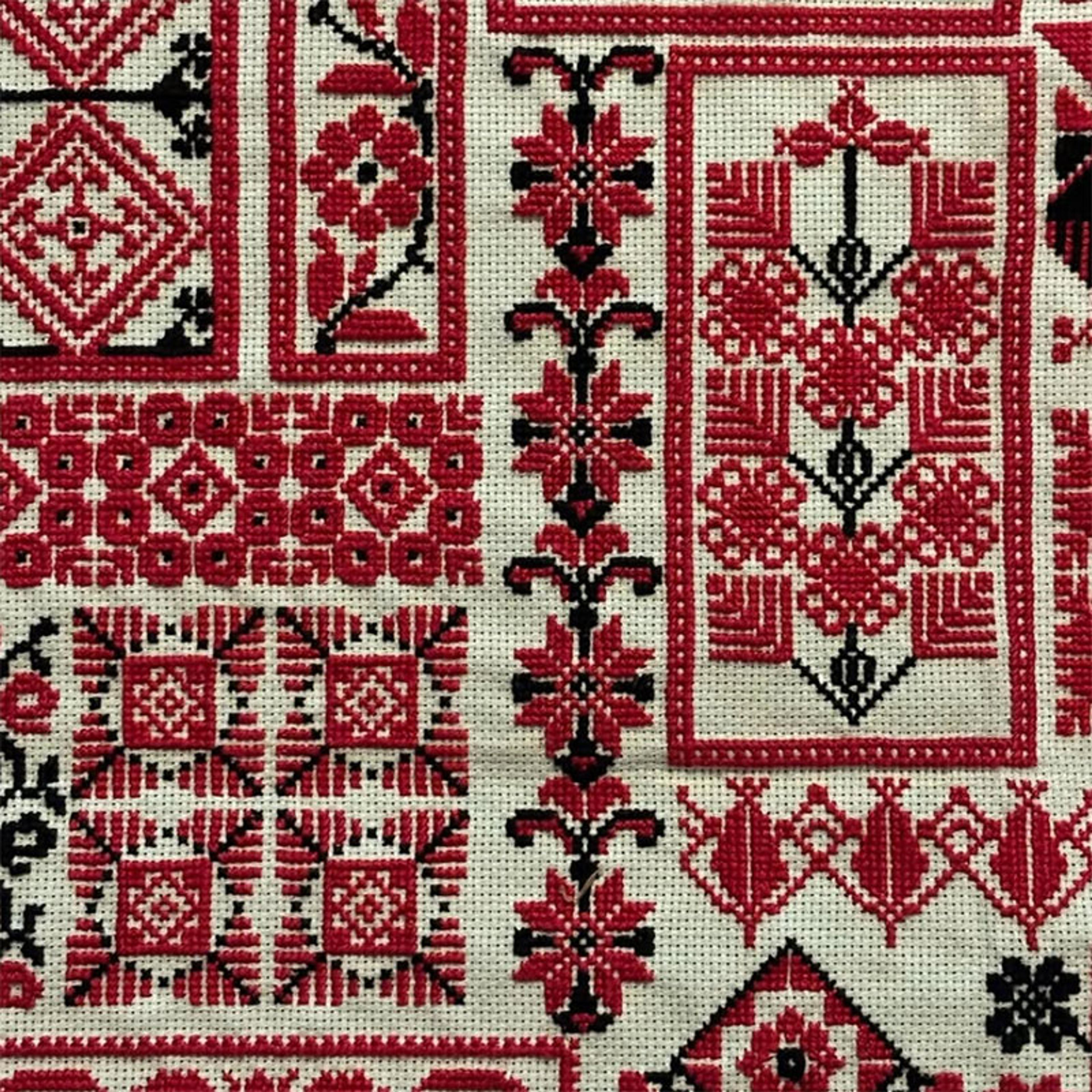Cross-stitch embroidery with red and black geometric floral patterns on a cream background.