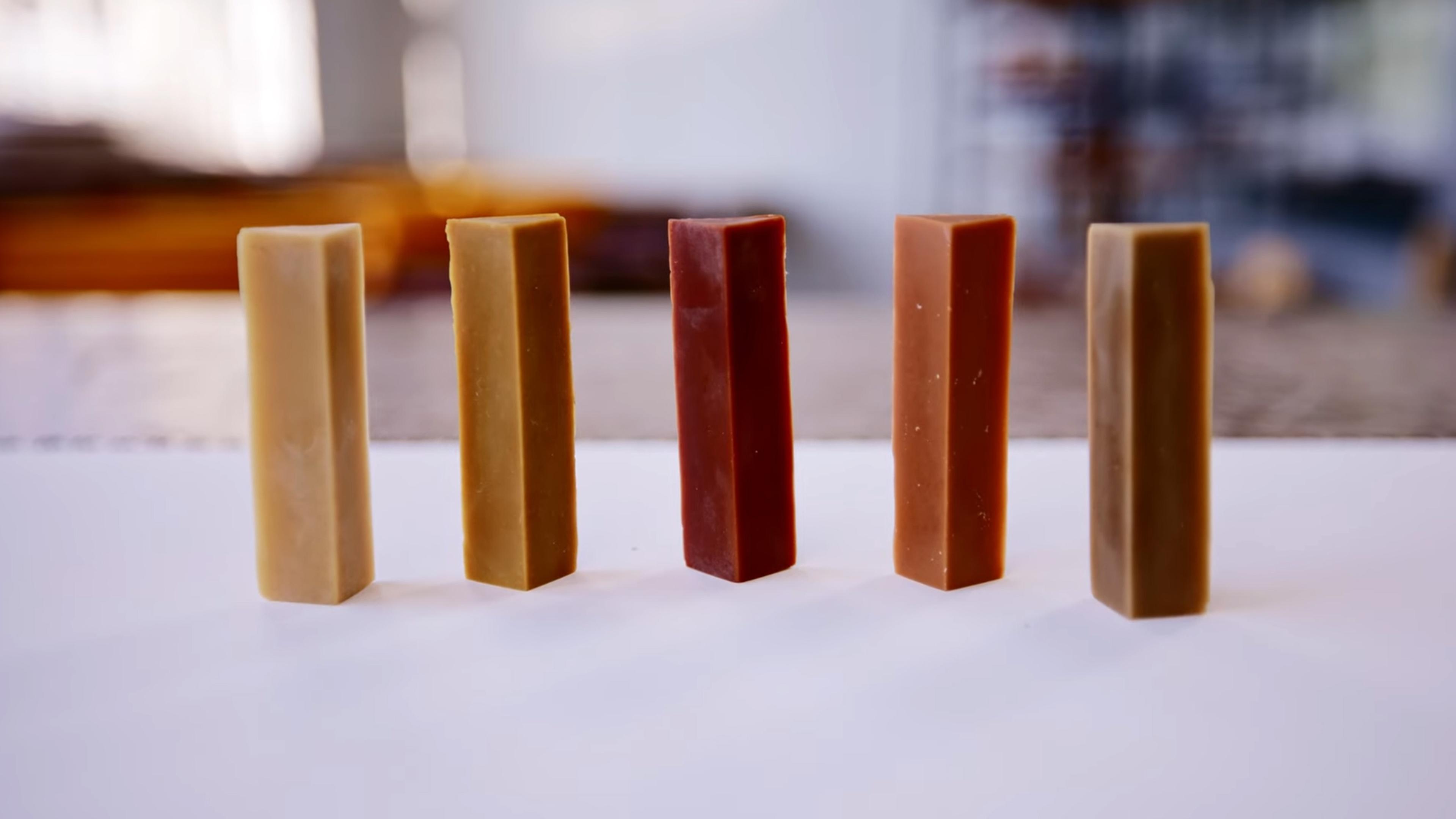 Five differently coloured triangular wax crayon bars standing upright on a white surface.