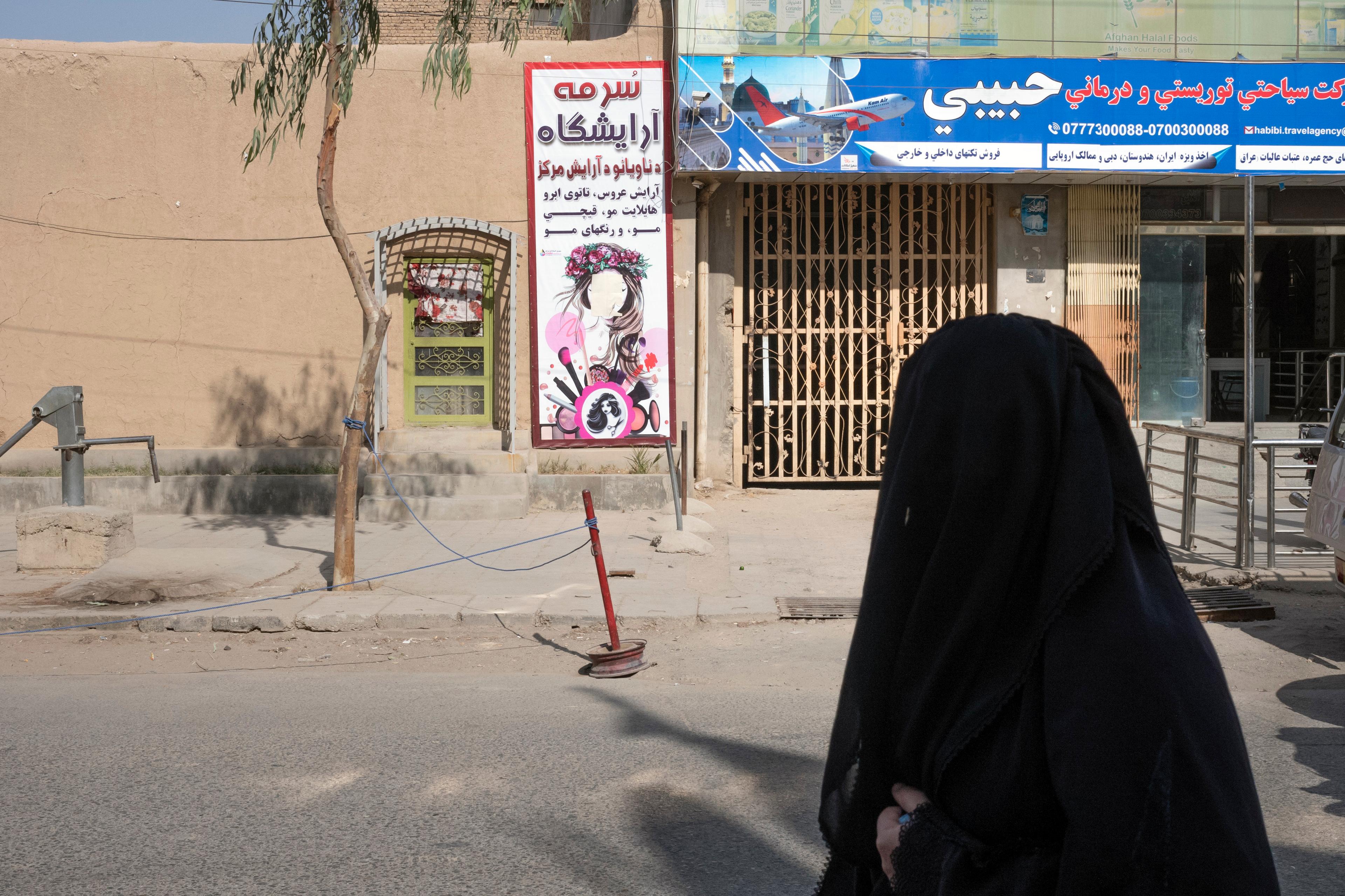 Photo of a woman in black clothing on a street near a beauty salon with a colourful sign and a travel agency.