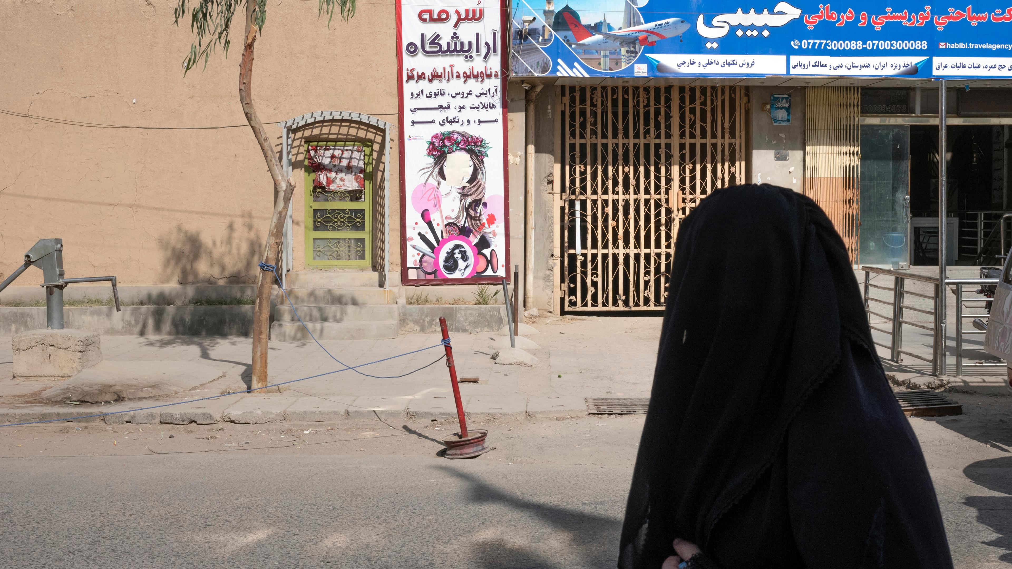 Photo of a woman in black clothing on a street near a beauty salon with a colourful sign and a travel agency.