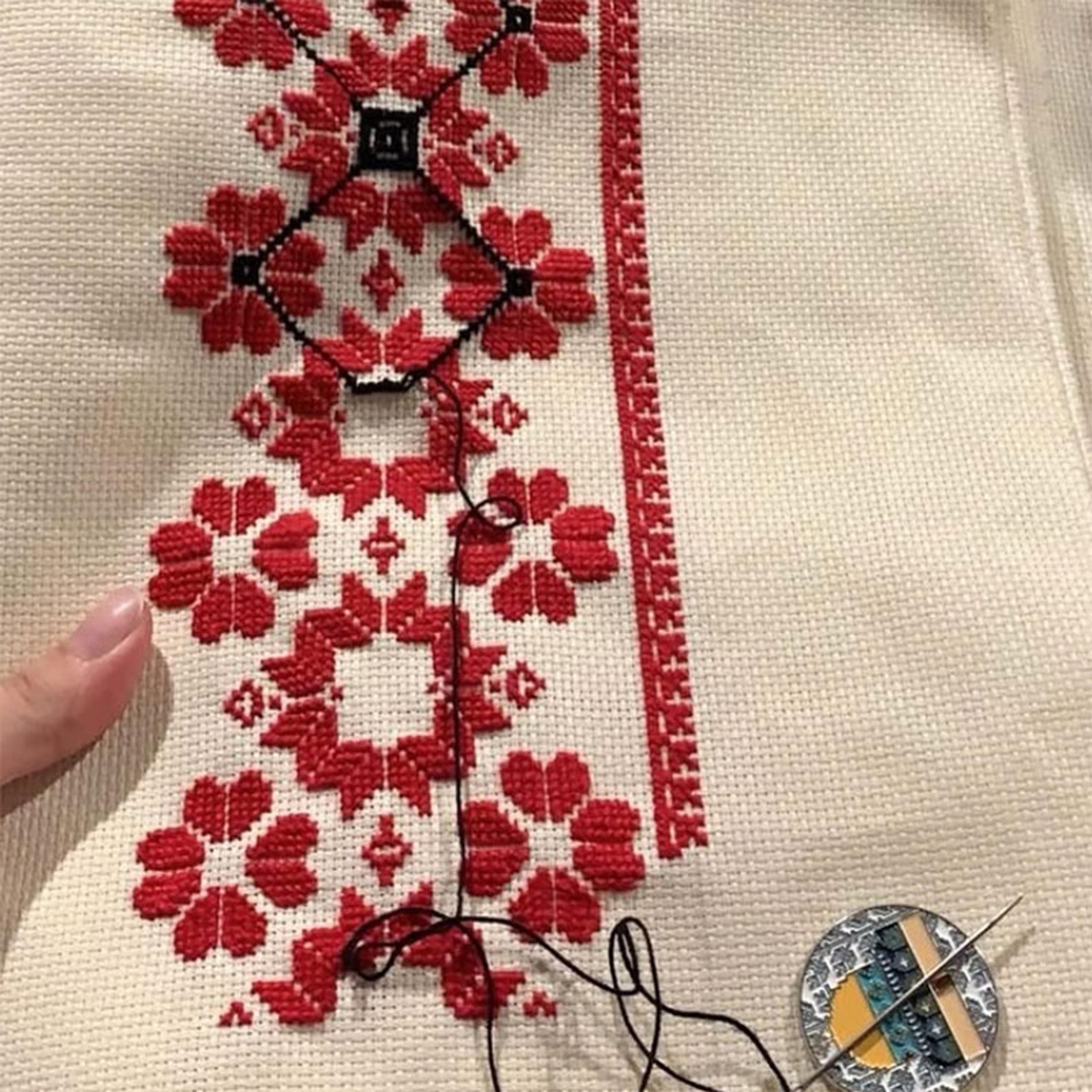 Photo of a cross-stitch embroidery in red and black geometric floral patterns on beige fabric with a needle and thread.