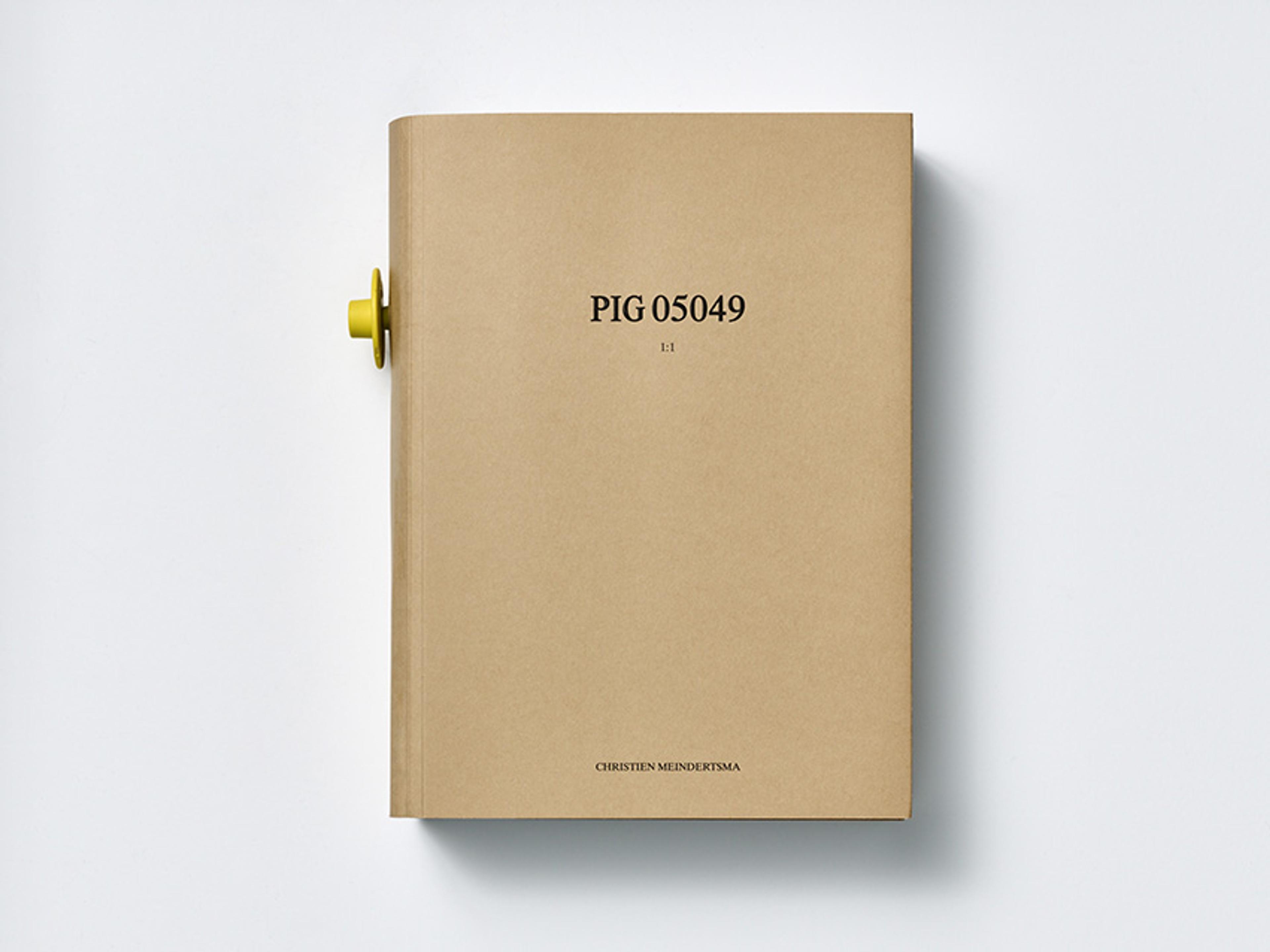 A closed beige book titled “PIG 05049” by Christien Meindertsma, with a yellow knob visible on the left side.