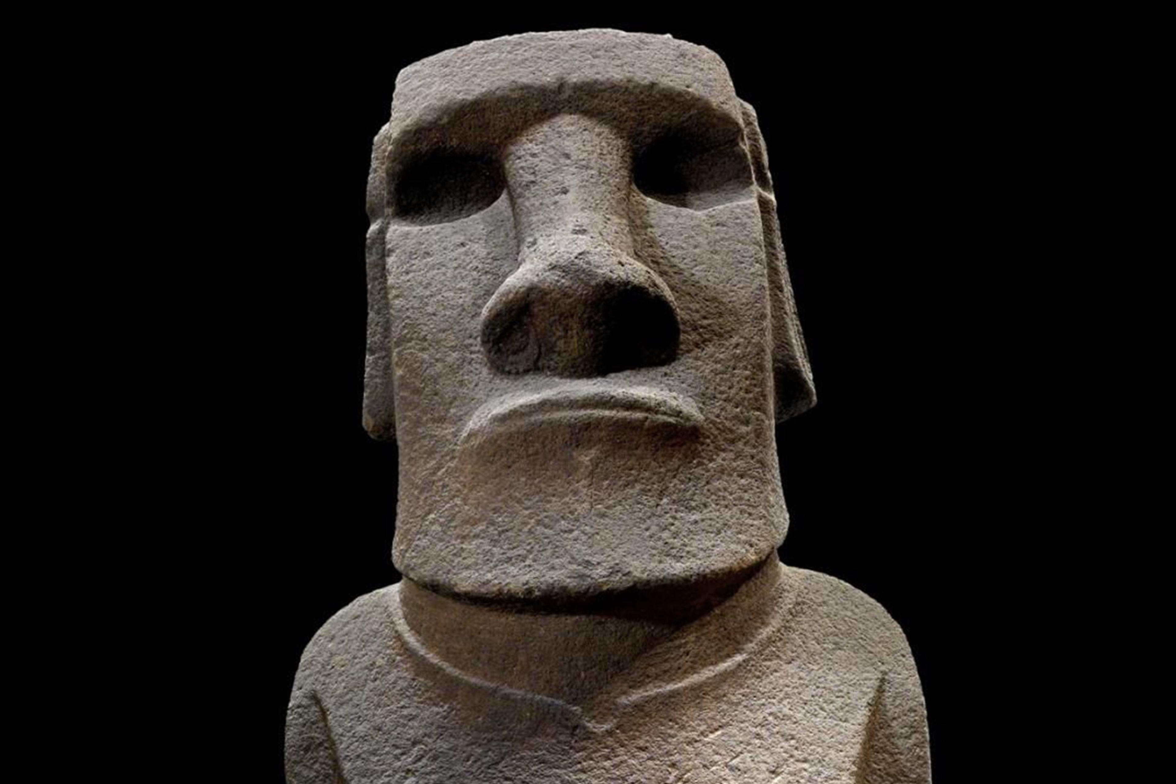 Stone statue of a Moai head with a prominent brow and nose against a black background, photo.