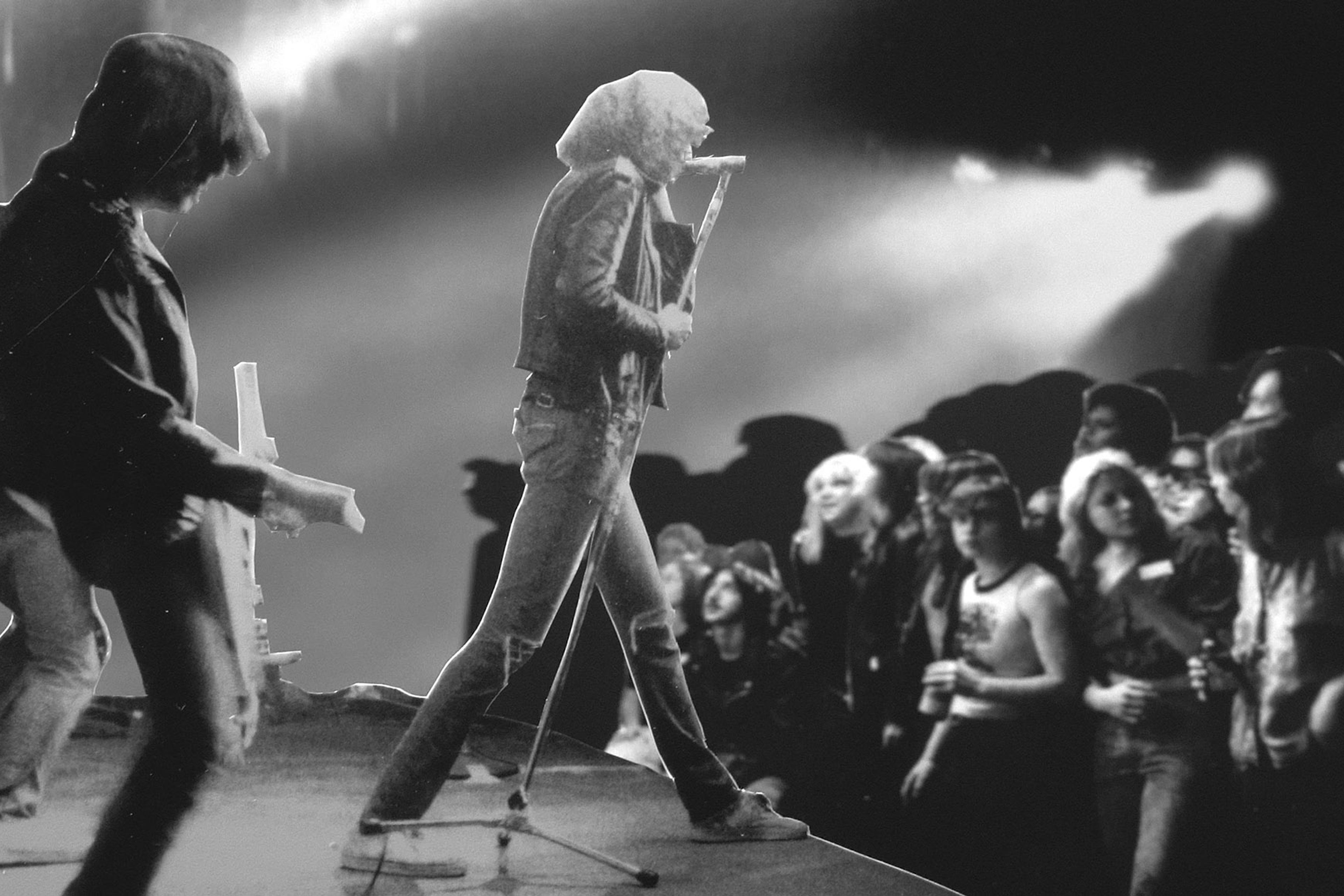 Black and white photo of a rock band performing on stage in front of a lively audience.