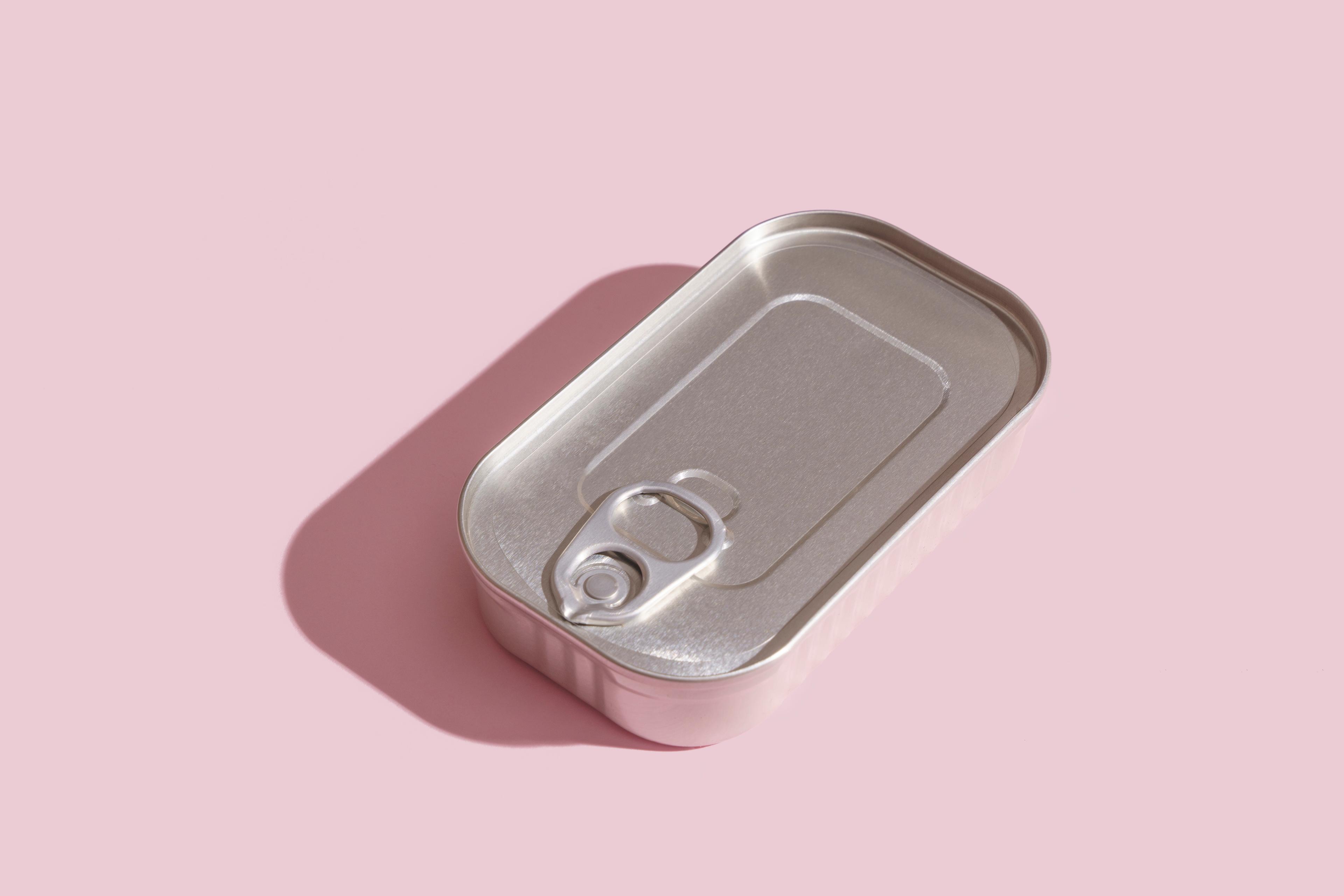 Photo of a closed metal tin can with a pull-tab lying on a pink background.