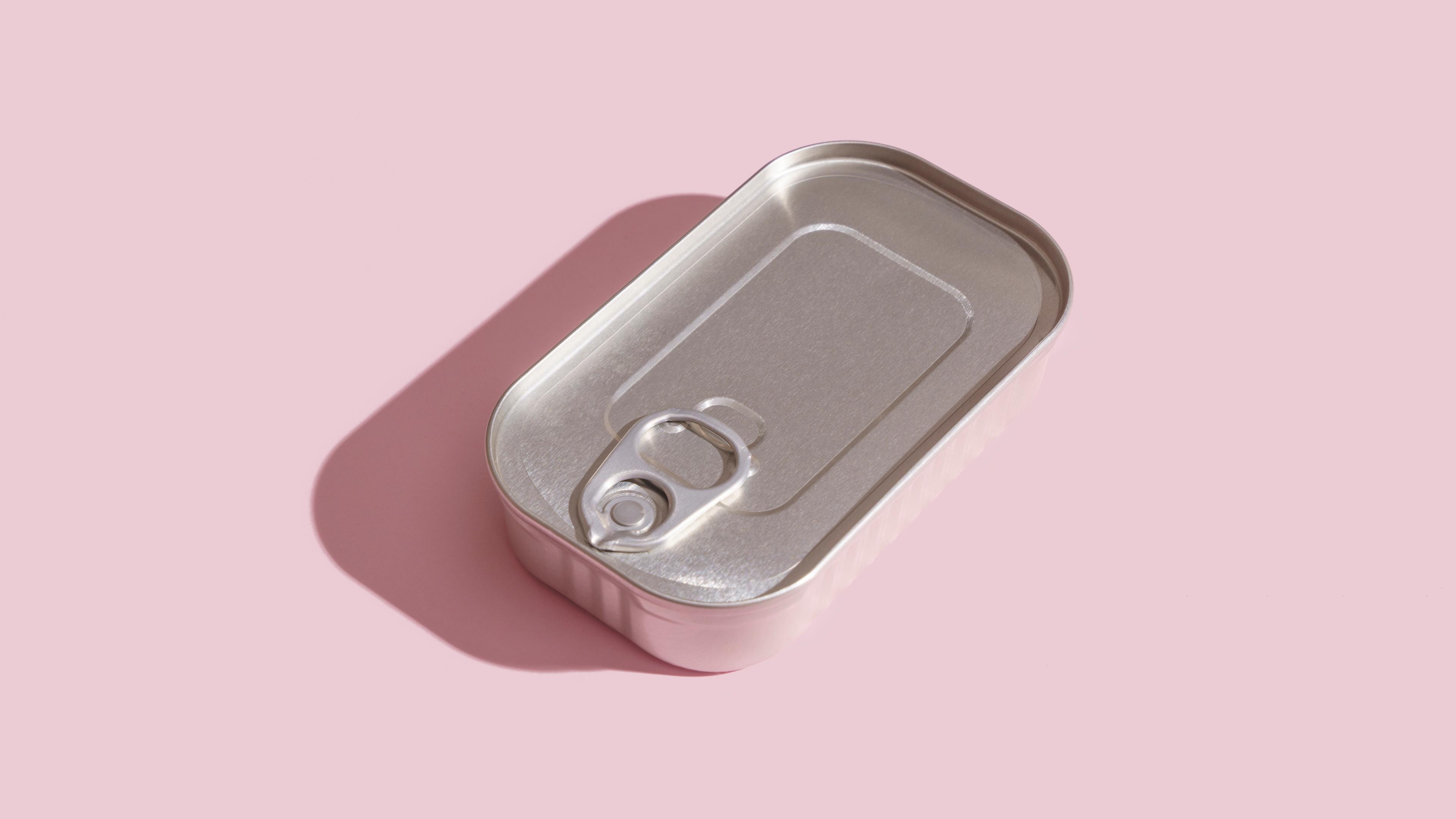Photo of a closed metal tin can with a pull-tab lying on a pink background.