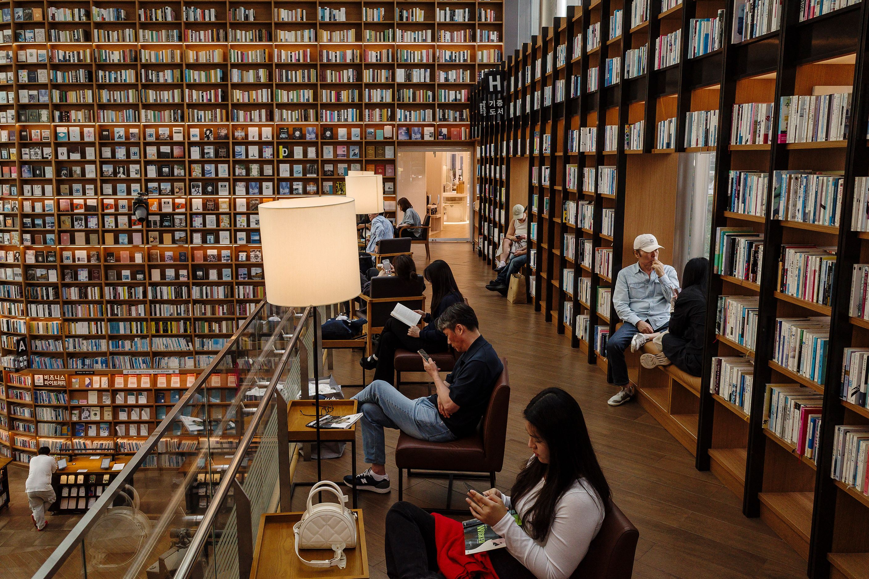A modern library with tall bookshelves and people reading or using devices in a cosy, well-lit atmosphere.