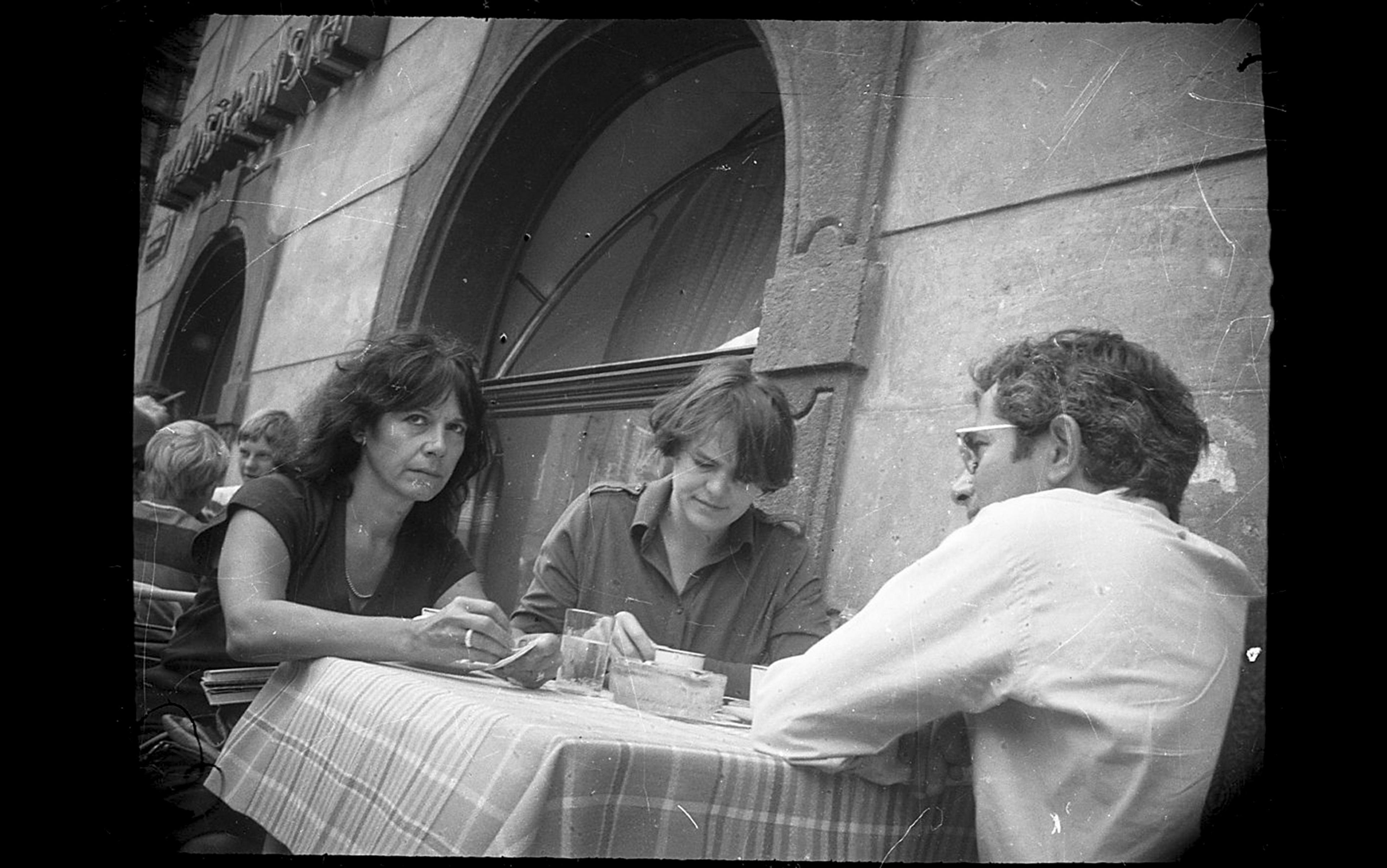 Black and white photo of three people seated at an outdoor café table.