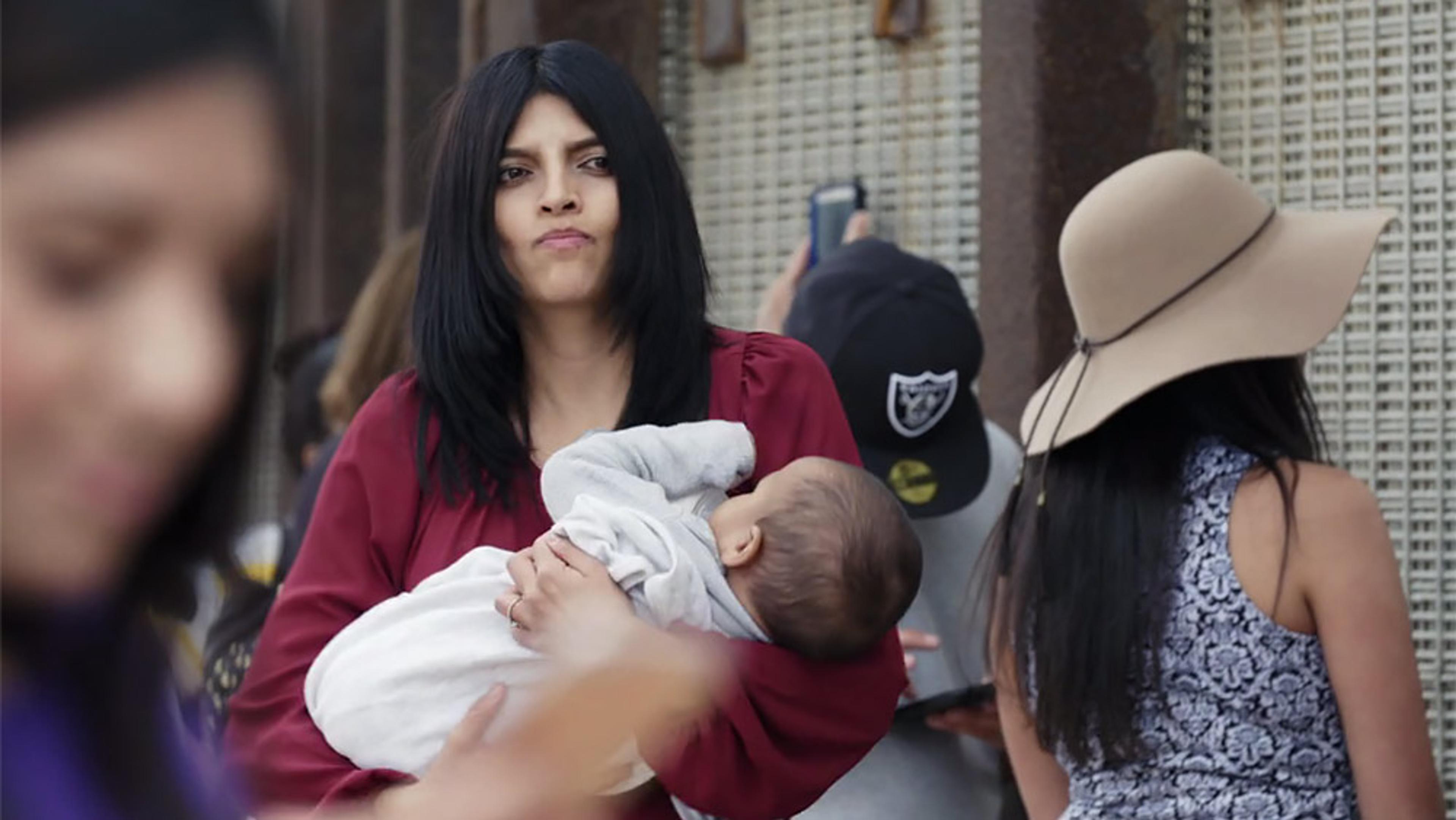 A woman in a red top holding a baby in a crowded outdoor setting.