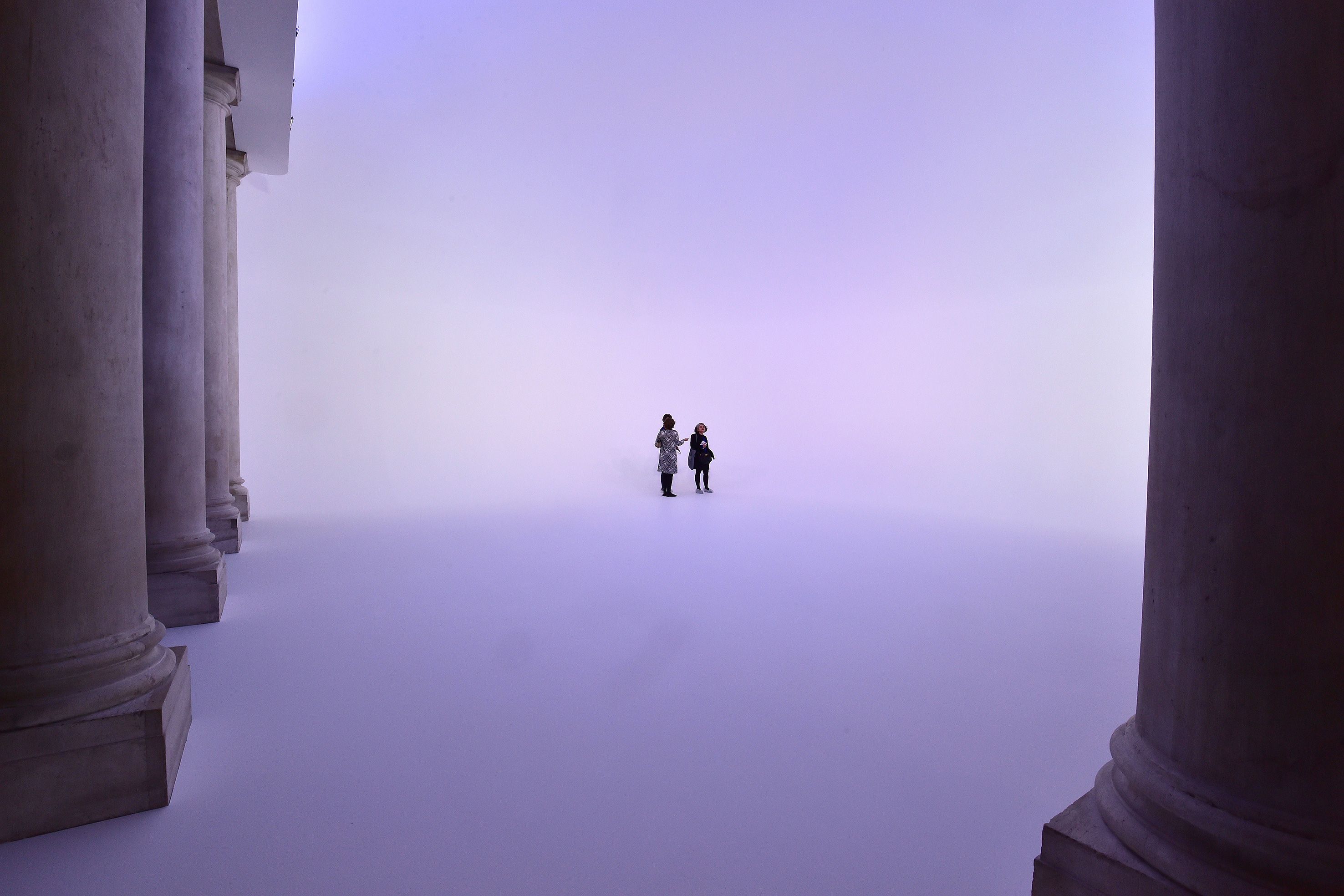Photo of two people standing in a purple haze between large columns in a vast, ethereal space.
