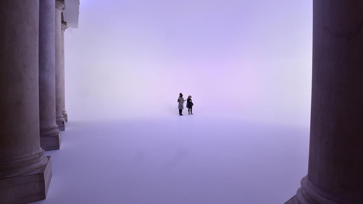 Photo of two people standing in a purple haze between large columns in a vast, ethereal space.