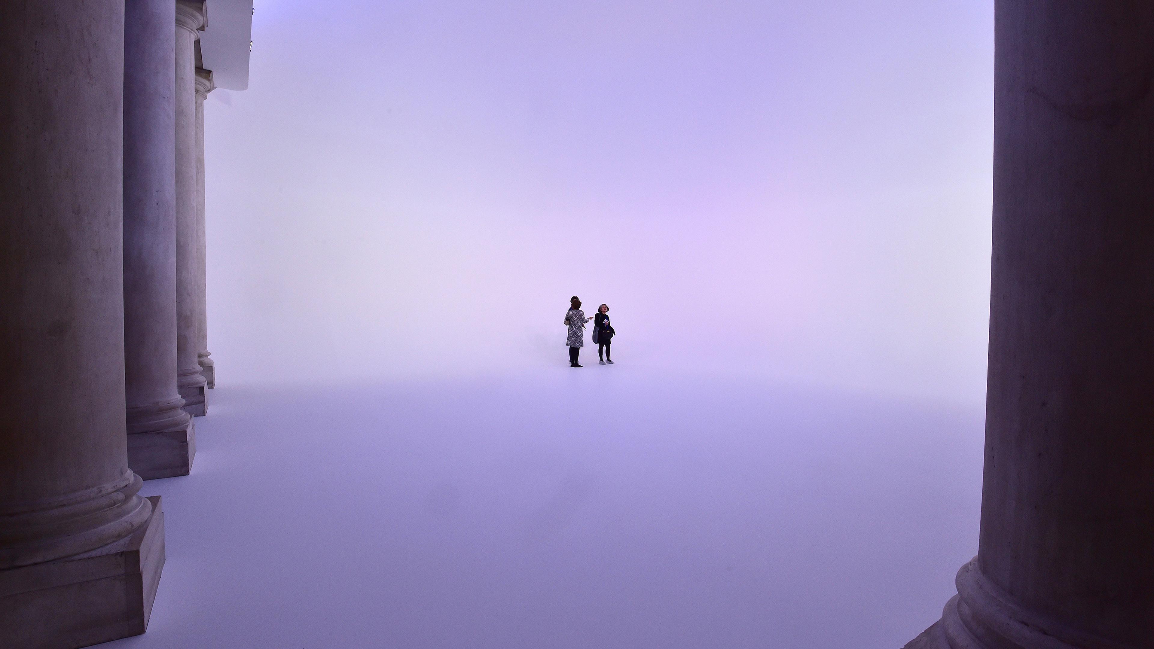 Photo of two people standing in a purple haze between large columns in a vast, ethereal space.