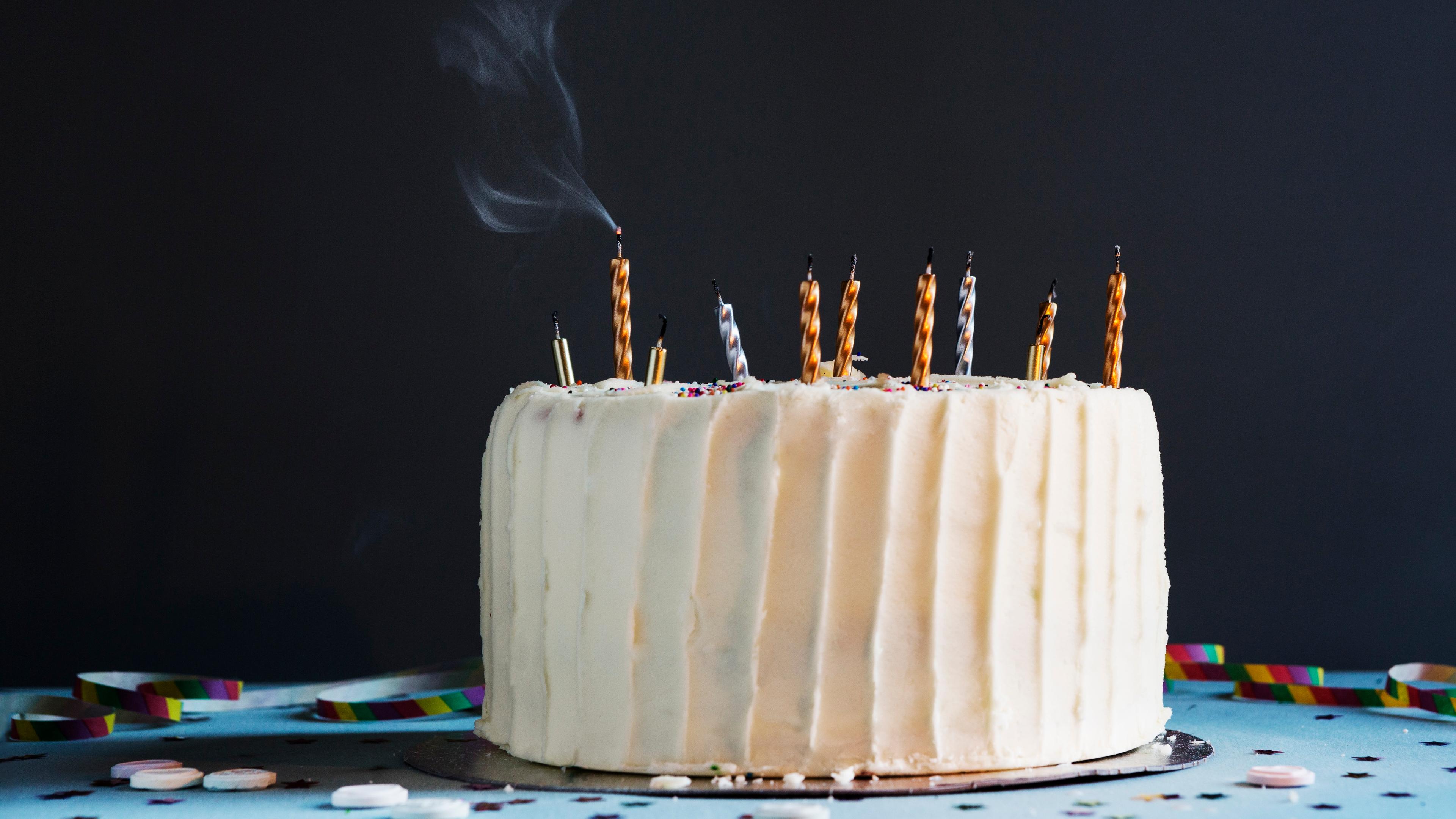 Photo of a cake with ten extinguished candles and smoke rising, set against a dark background on a decorated table.