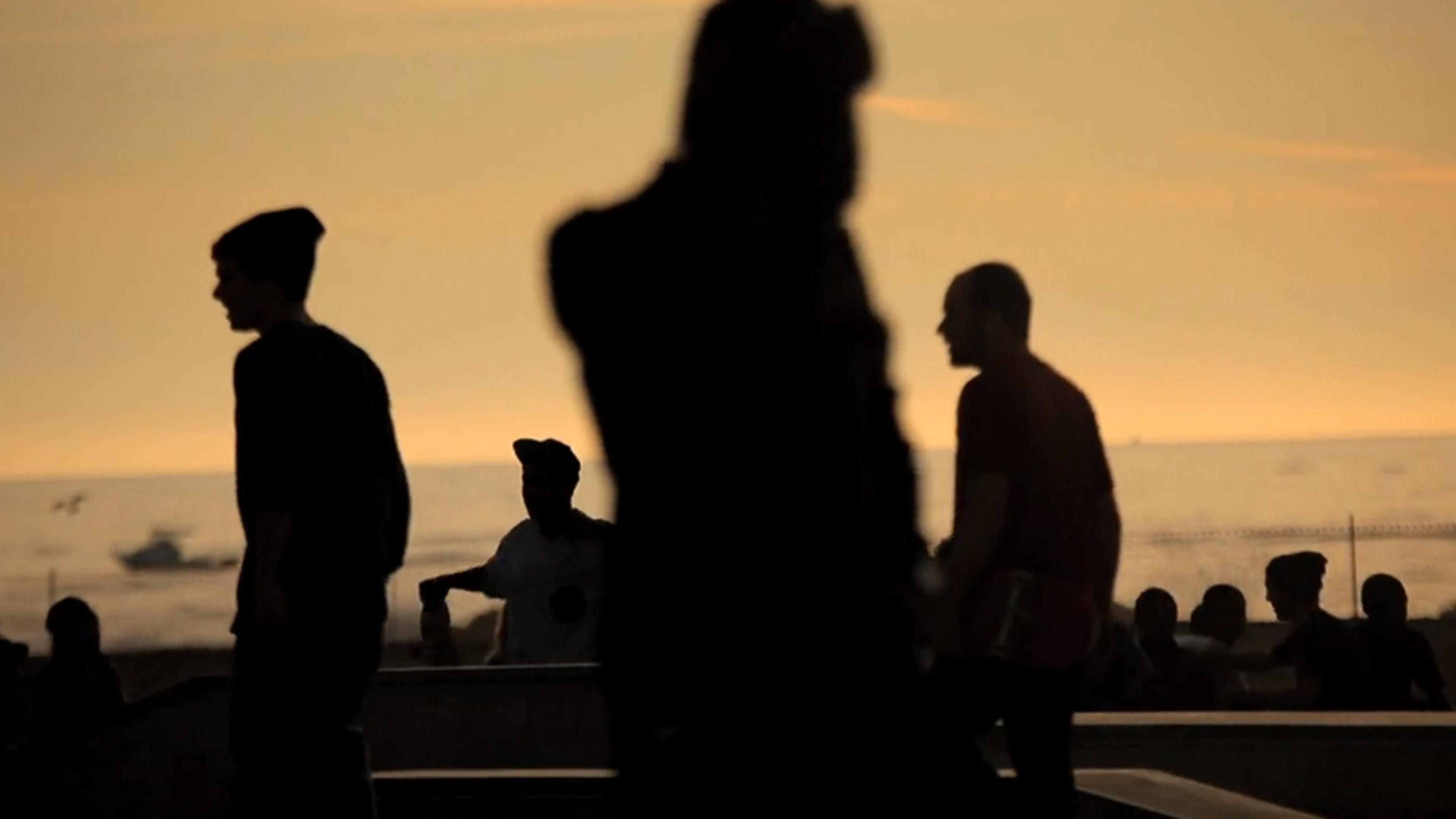 Silhouettes of people at a skatepark during sunset, with an ocean in the background.