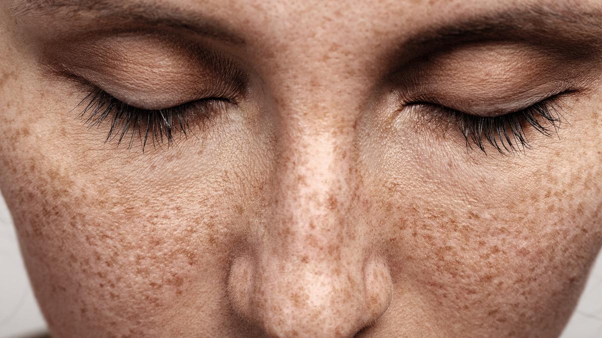 Close-up photo of a person’s face with closed eyes and freckles on their skin.