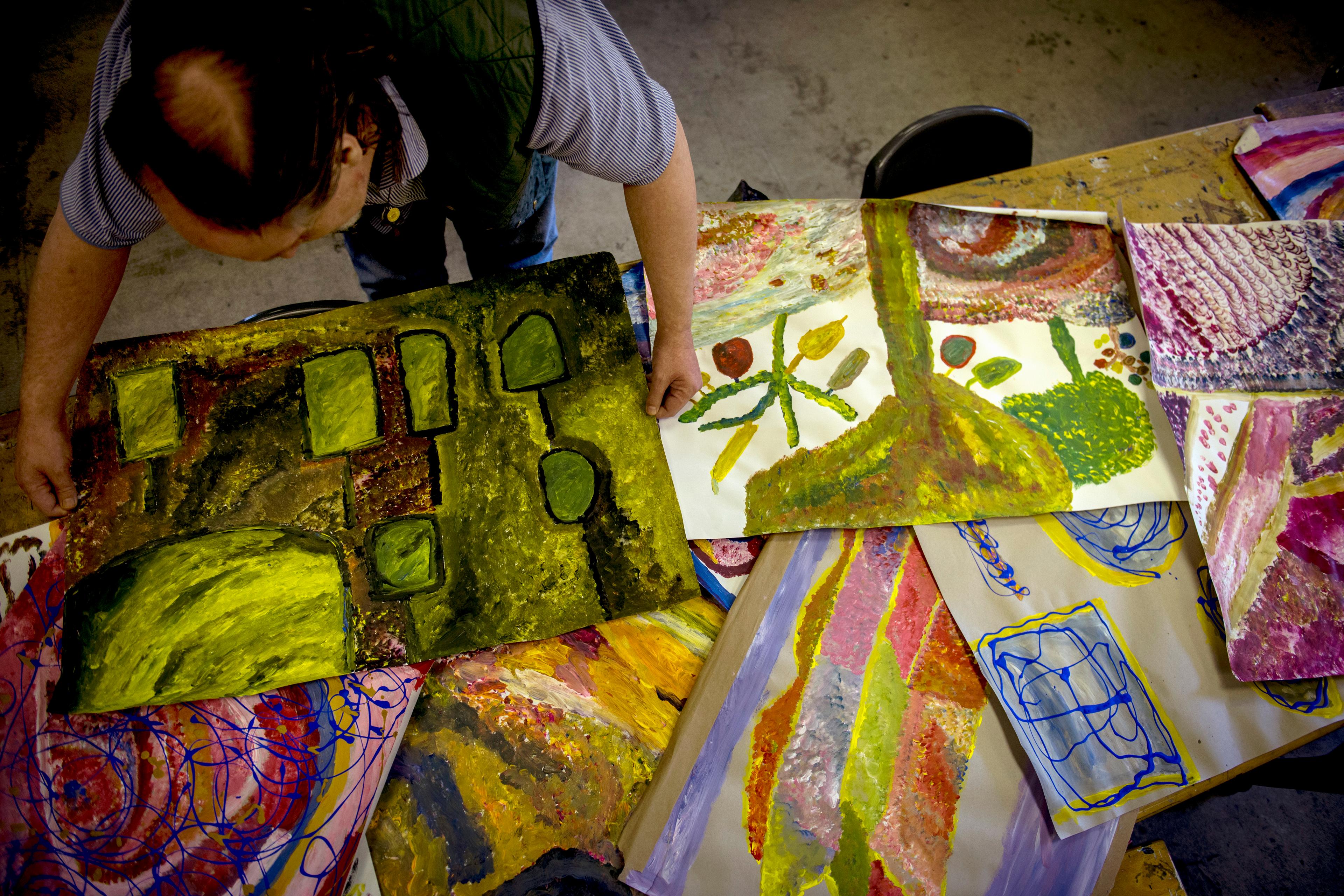 Person arranging colourful abstract paintings on a table, viewed from above.