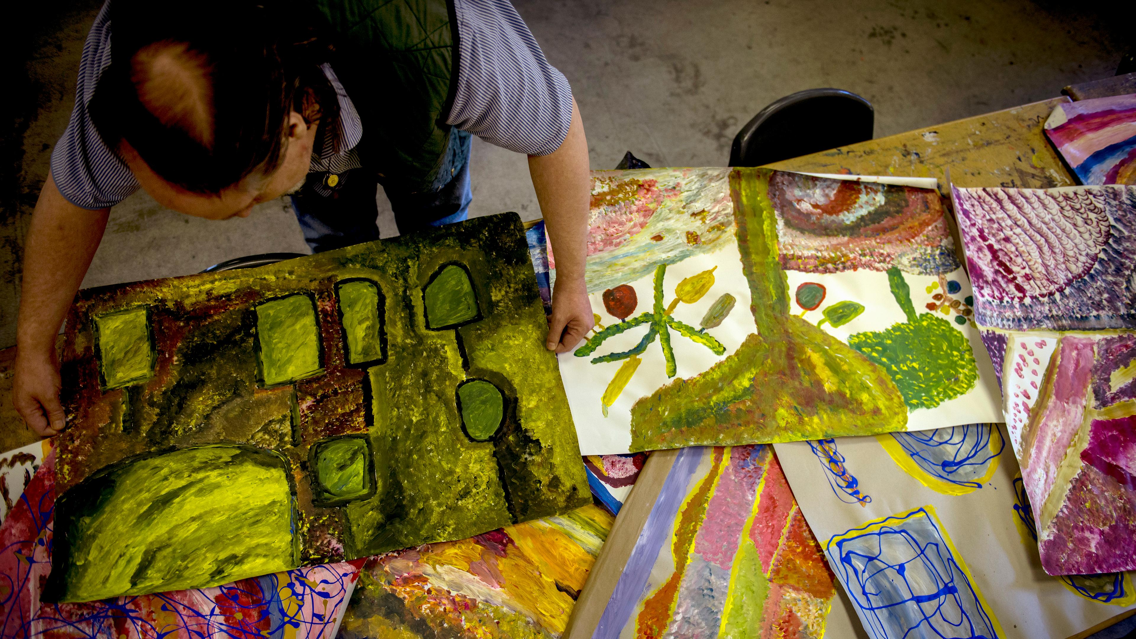 Person arranging colourful abstract paintings on a table, viewed from above.