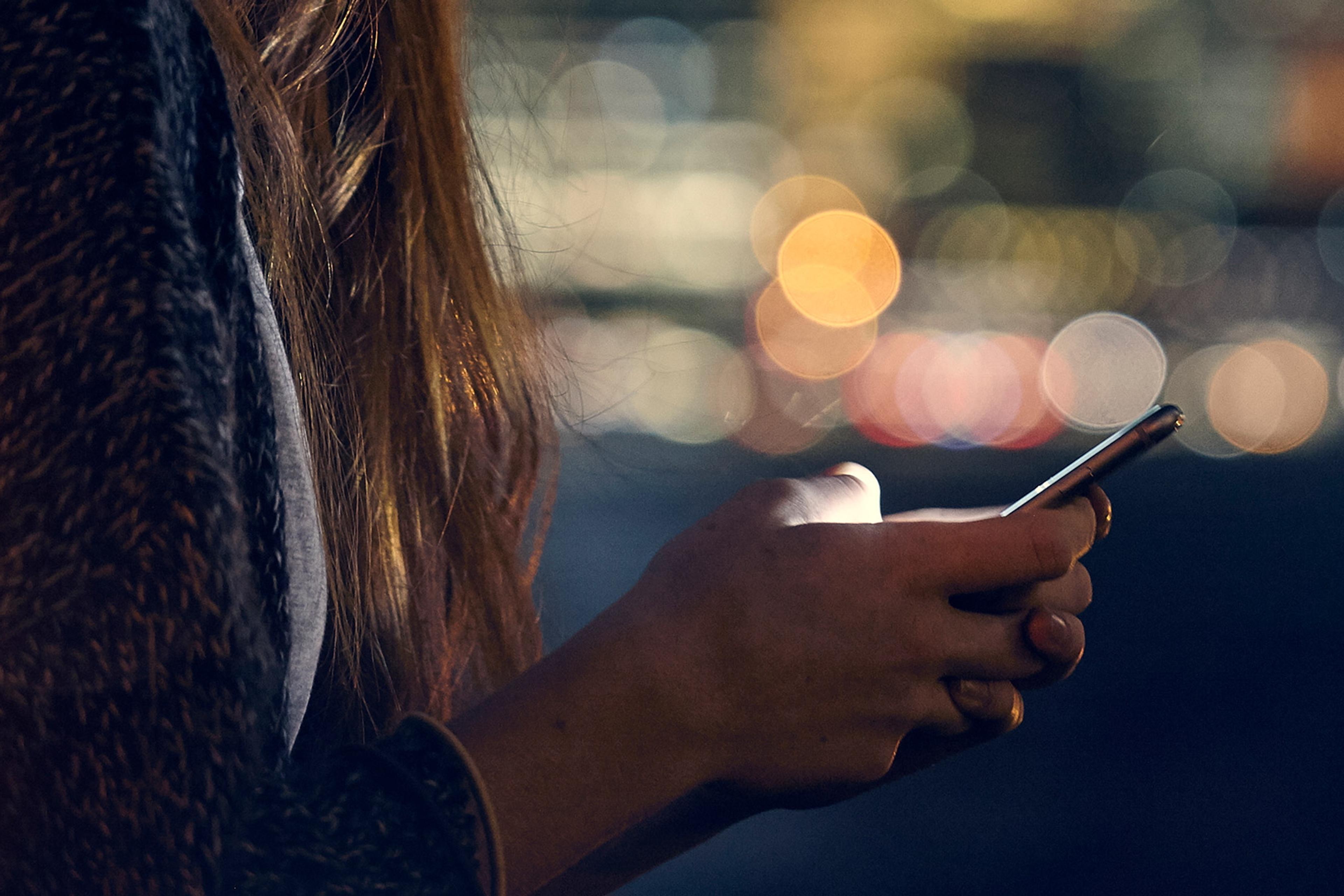 Close-up of a person’s hands using a smartphone at night, with blurred city lights in the background.